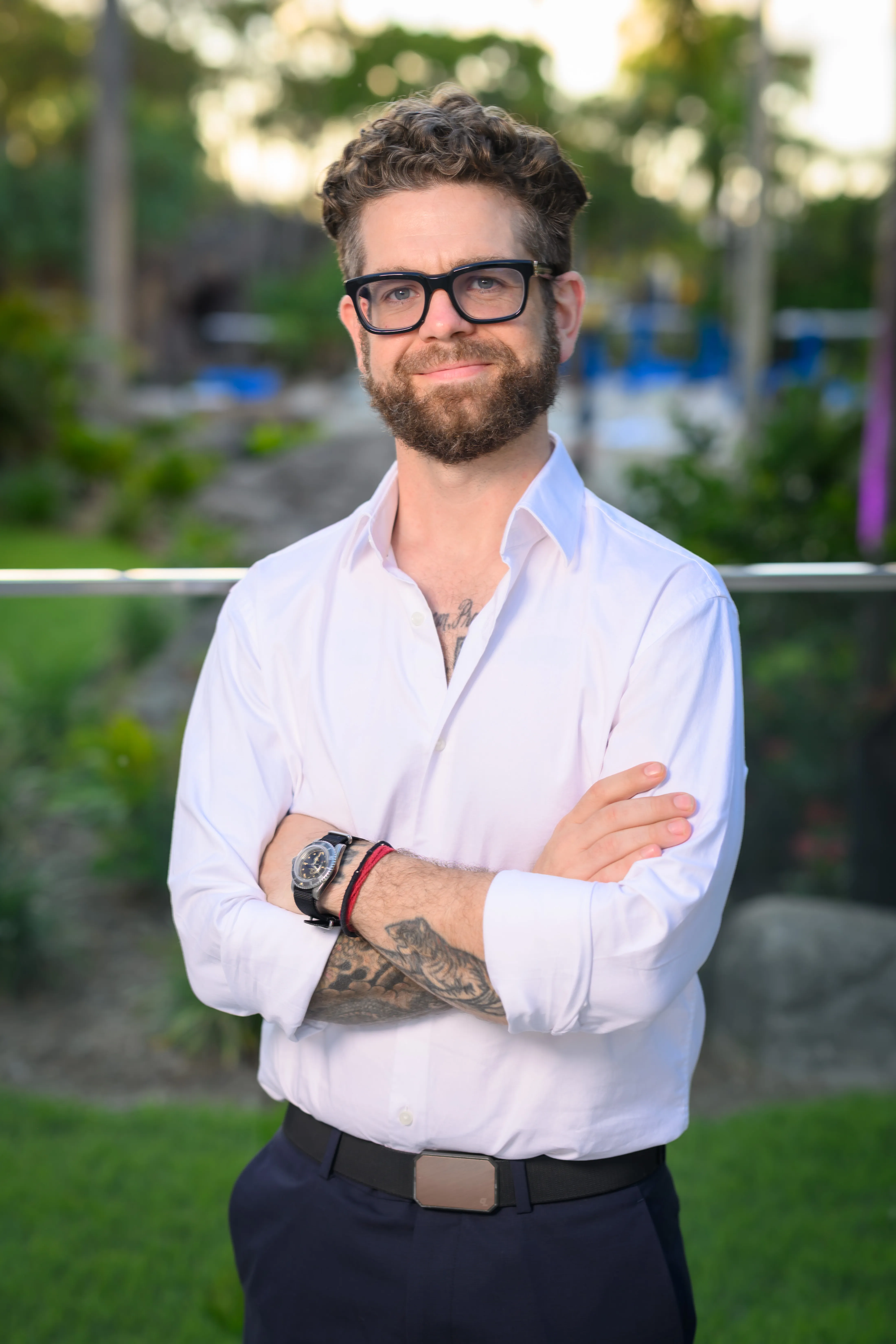 Jack Osbourne, wearing a white shirt and black-framed glasses, poses with his arms crossed.
