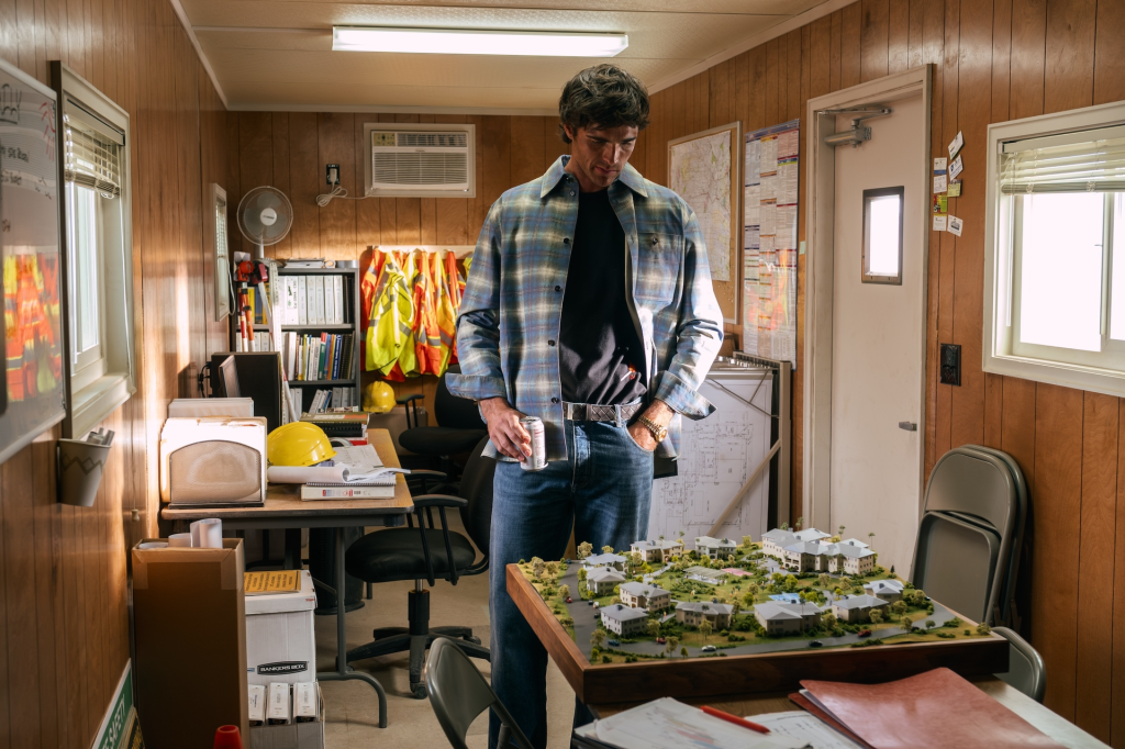 Jacob Elordi as Nate Jacobs in Euphoria Season 3 standing next to a miniature model of houses.
