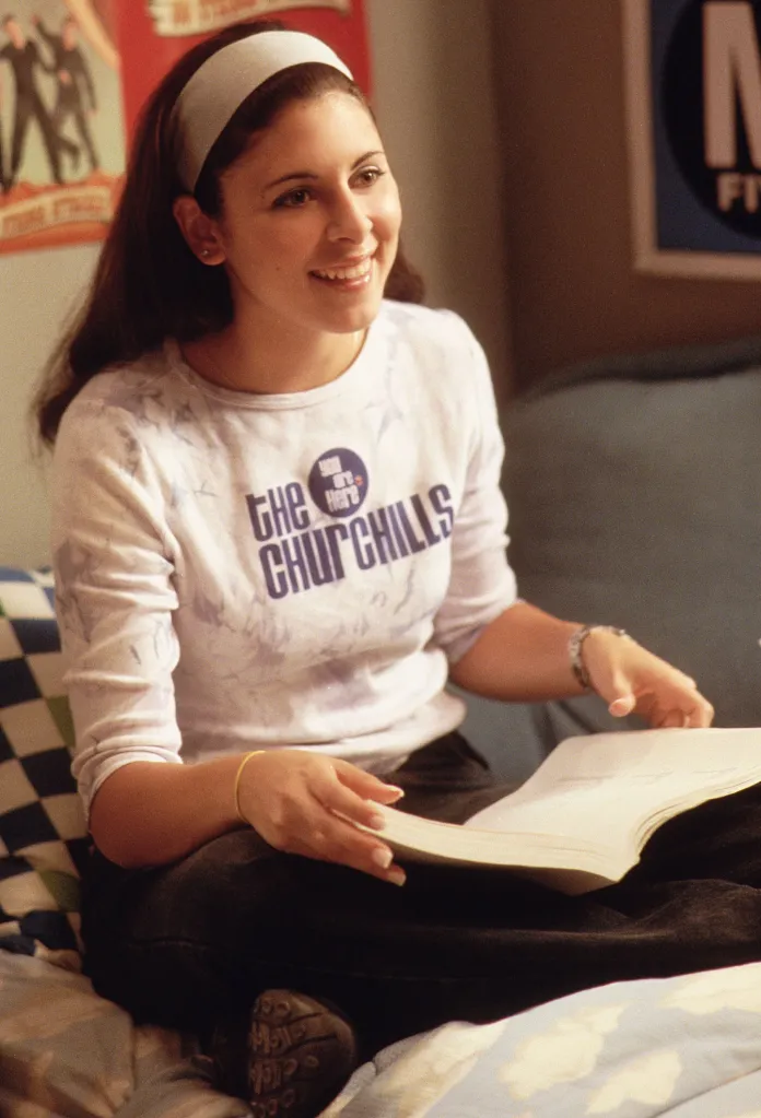 Jamie-Lynn Sigler as Meadow Soprano smiles while sitting with a book in "The Sopranos."