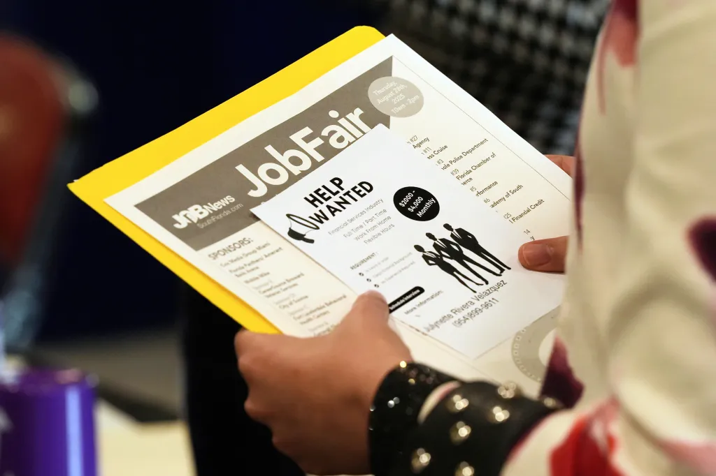 A person holding a flyer for a job fair with "Job Fair" and "Help Wanted" visible.