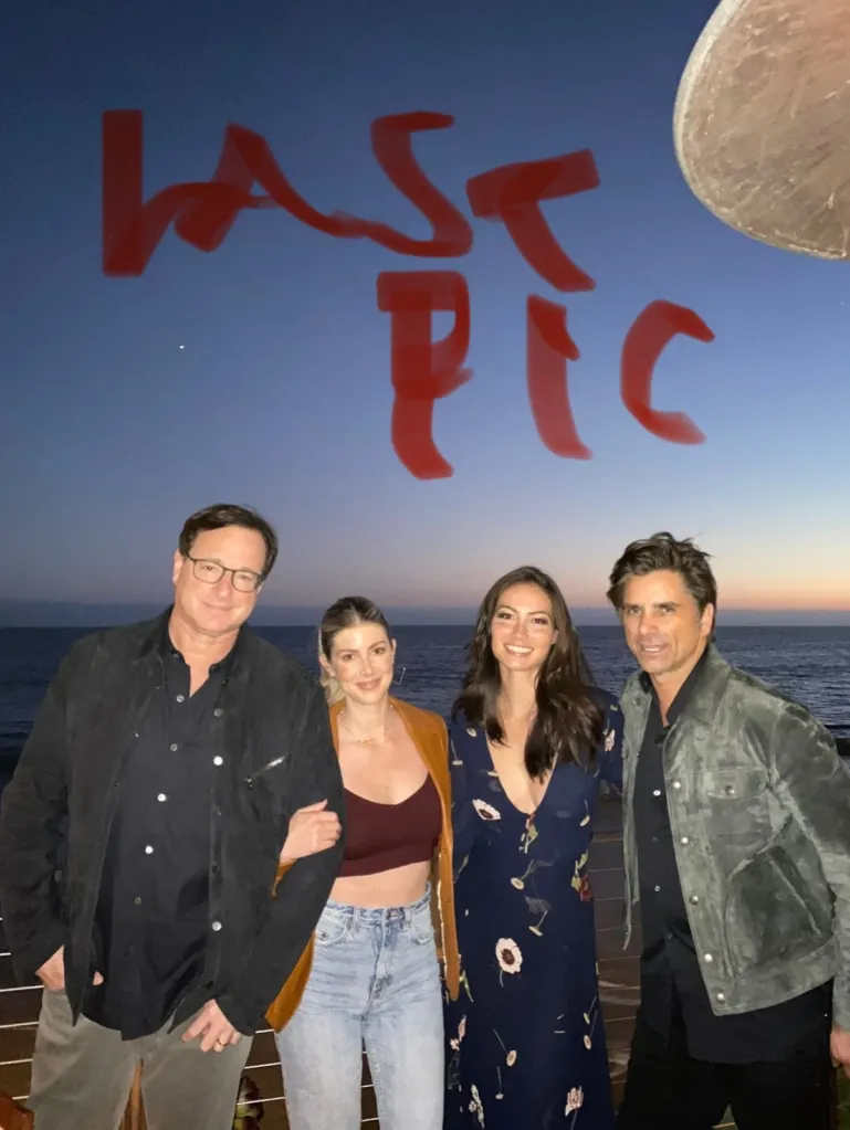 Bob Saget and John Stamos with two women, standing by the ocean at sunset, with the words "LAST PIC" written in red across the sky.