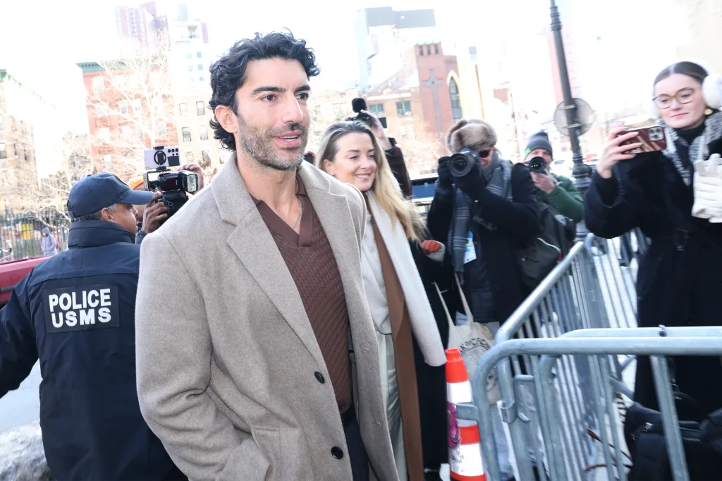 Justin Baldoni entering federal court in Manhattan, surrounded by photographers and a police officer.