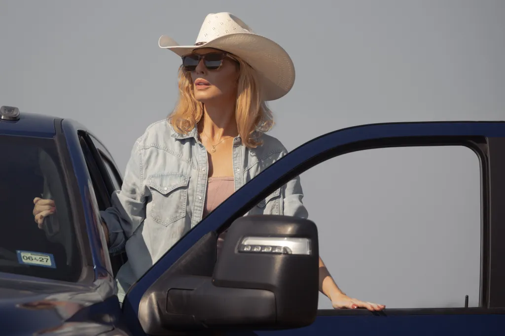 Kelly Reilly as Beth Dutton wearing a cowboy hat and sunglasses, leaning out of a blue pickup truck.