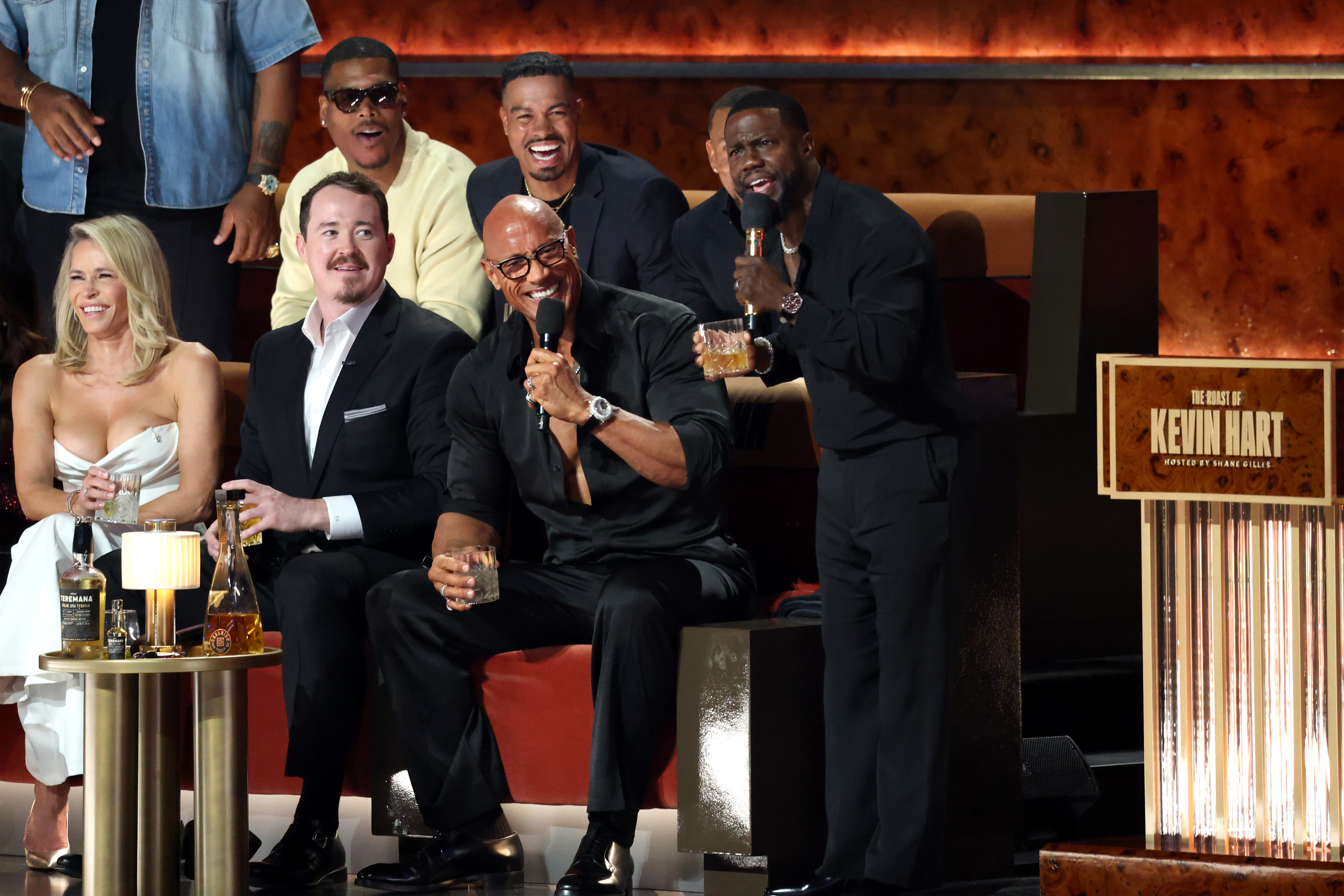 Kevin Hart holding a microphone while Dwayne "The Rock" Johnson laughs during "The Roast of Kevin Hart" at the Netflix Is A Joke Festival.