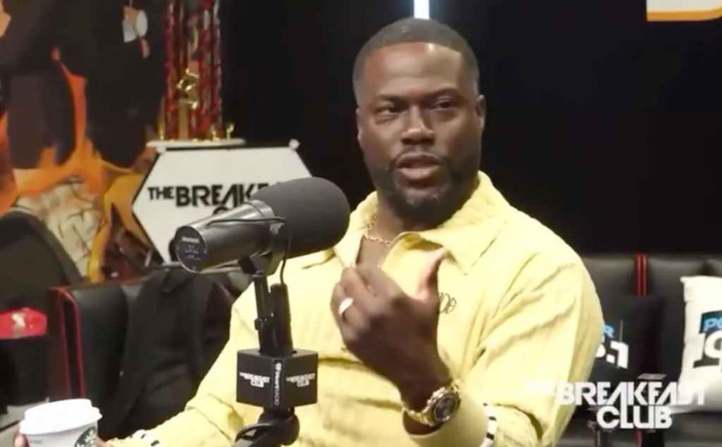 Kevin Hart speaking into a microphone, holding a coffee cup, at The Breakfast Club.