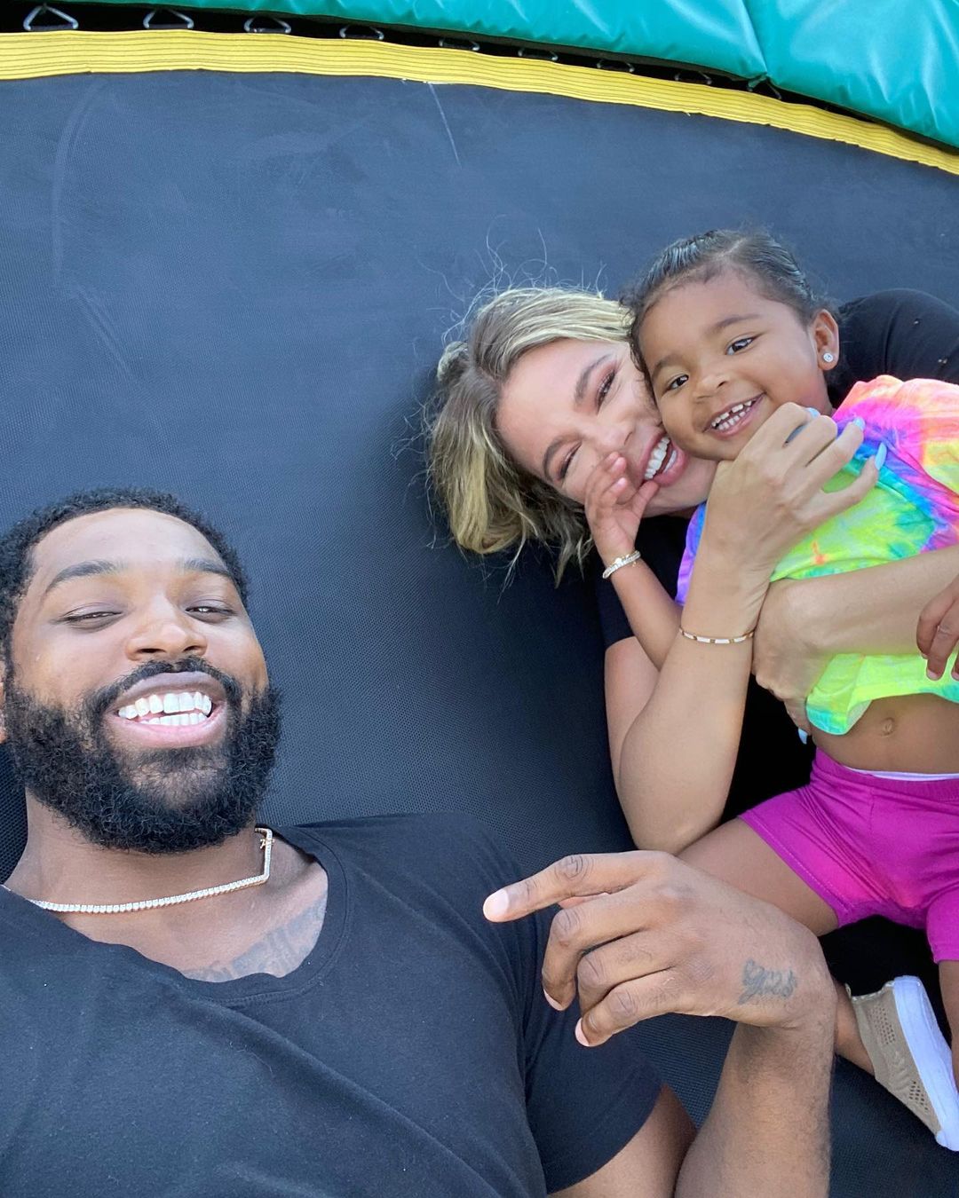 Khloe Kardashian, Tristan Thompson, and their daughter True lying on a trampoline.
