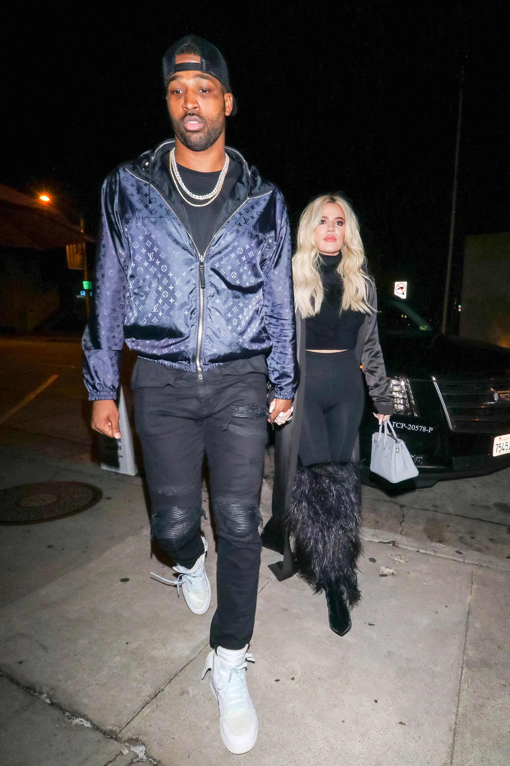 Khloe Kardashian and Tristan Thompson walk together at night.