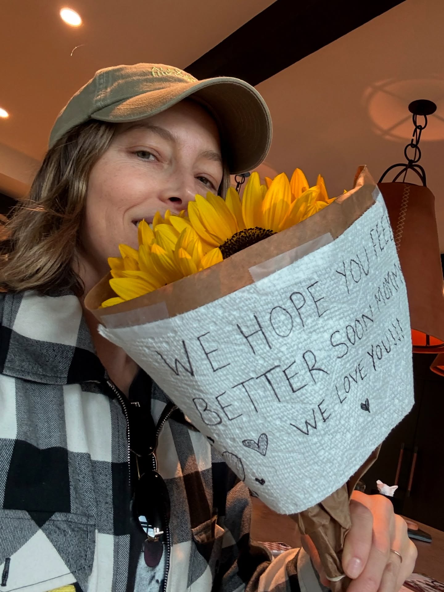 Jessica Biel holding a bouquet of sunflowers with a note that says "We hope you feel better soon, Mama! We love you!"
