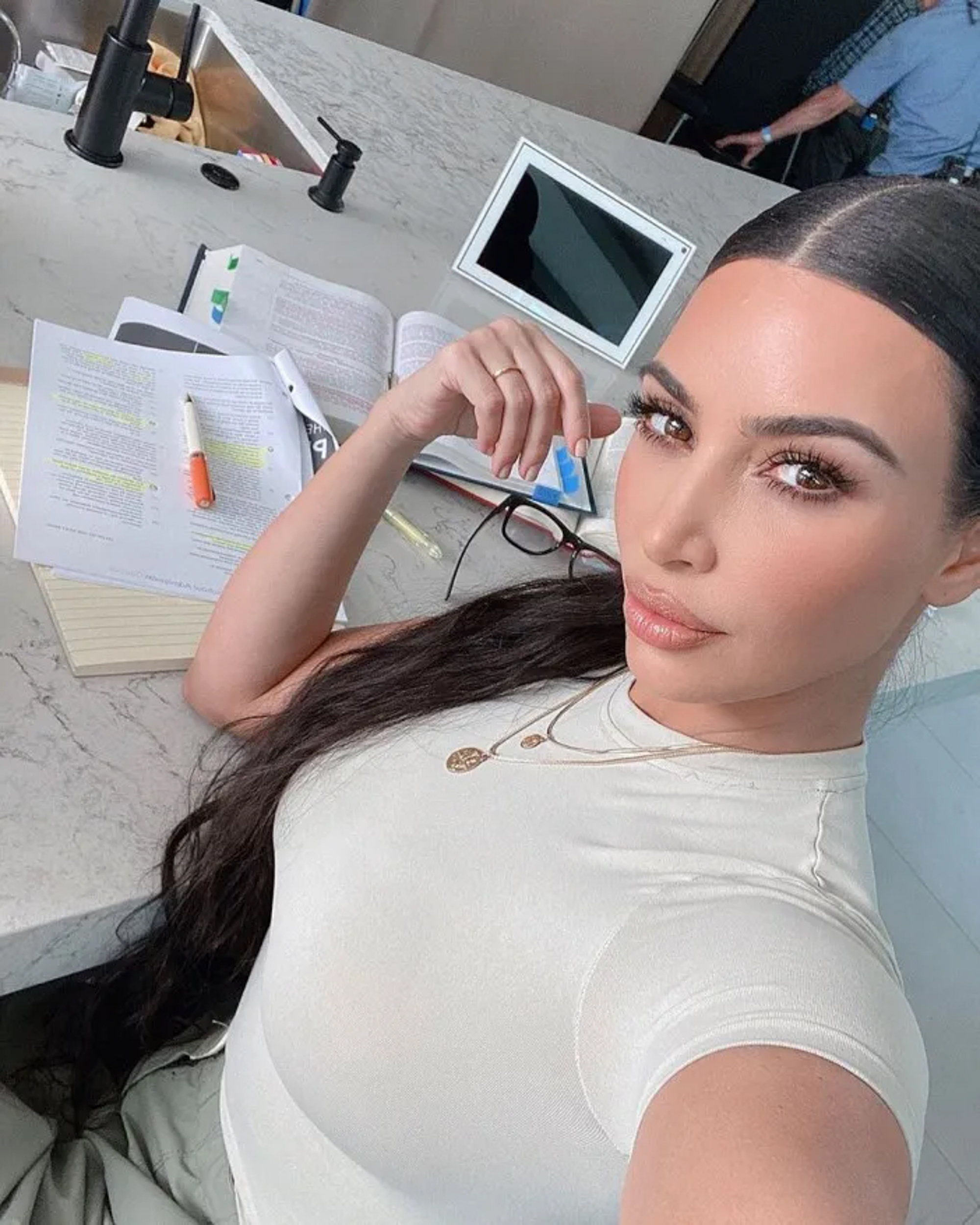 Kim Kardashian studying for the bar exam at a marble counter, with books, papers, and a highlighter surrounding her.