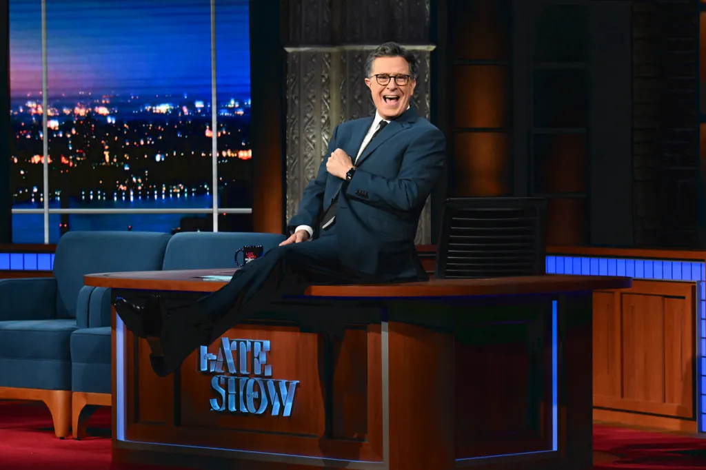 Stephen Colbert sitting on his desk on the set of The Late Show.