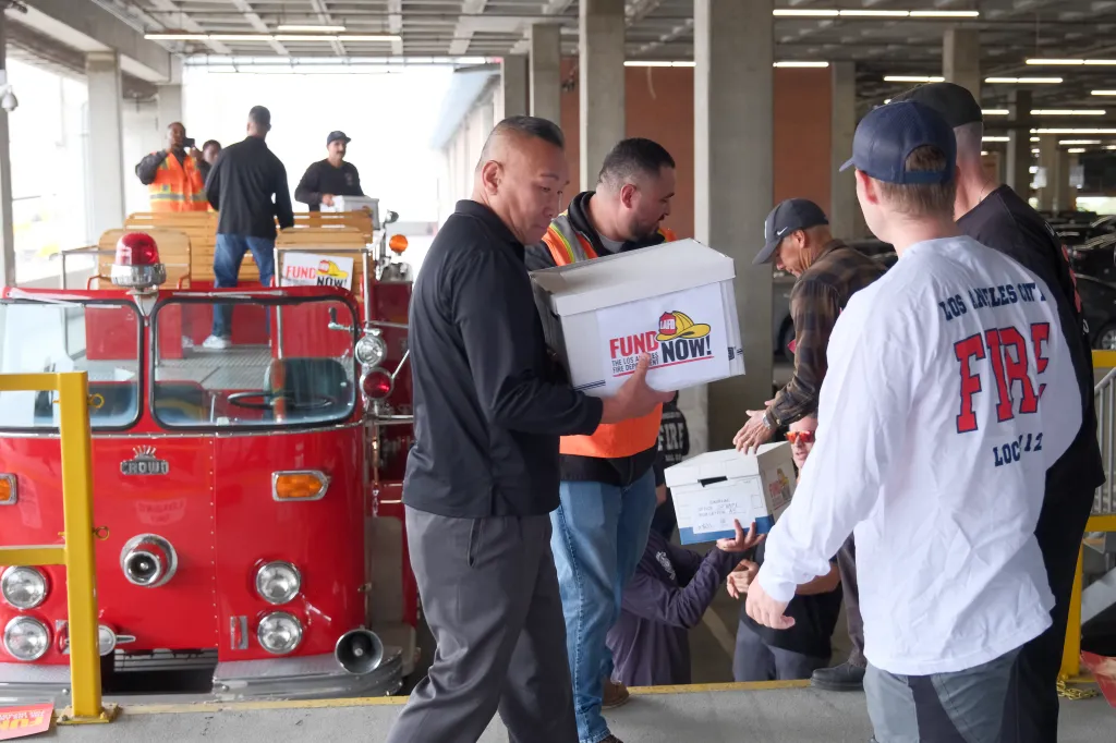 People gather with boxes of petitions that read "Fund LAFD Now!" in front of a fire engine.