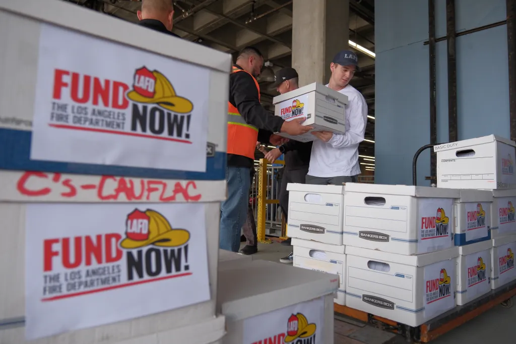 Boxes labeled "Fund the Los Angeles Fire Department Now!" being loaded onto a cart.