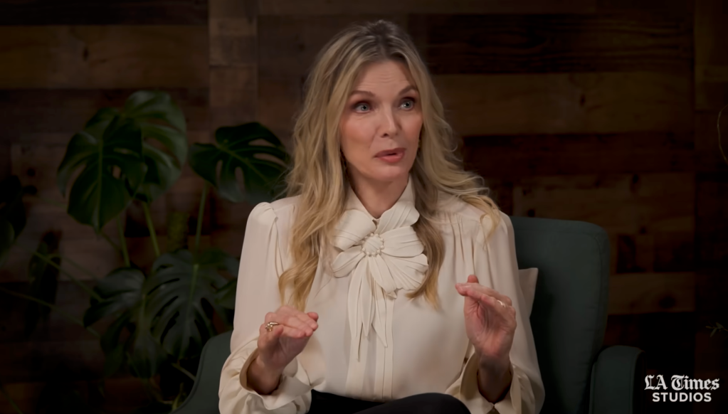 Madison, a woman with long blonde hair, wears a cream-colored blouse with a large floral embellishment and gestures with her hands.