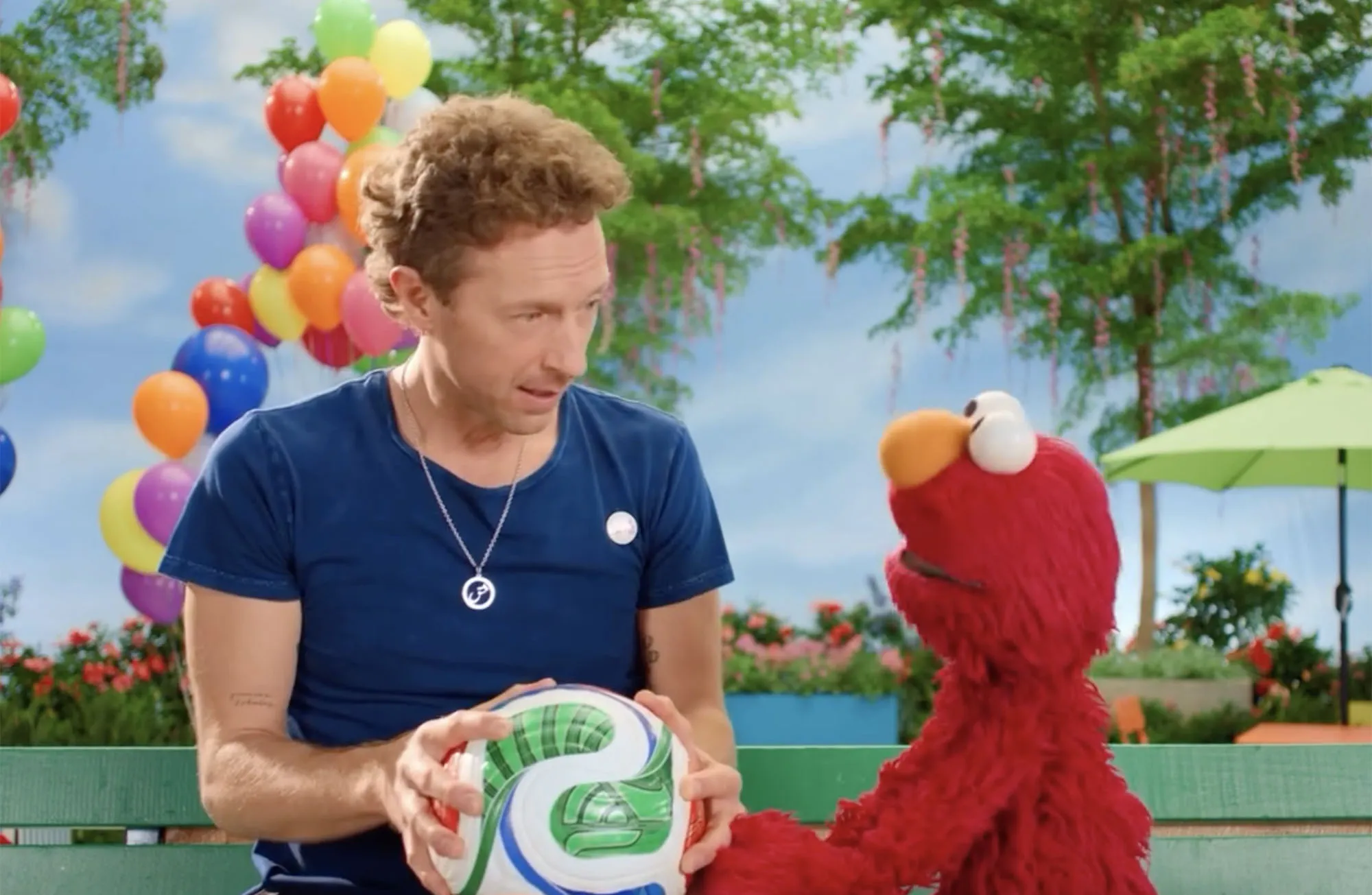 Chris Martin holding a soccer ball with Elmo.