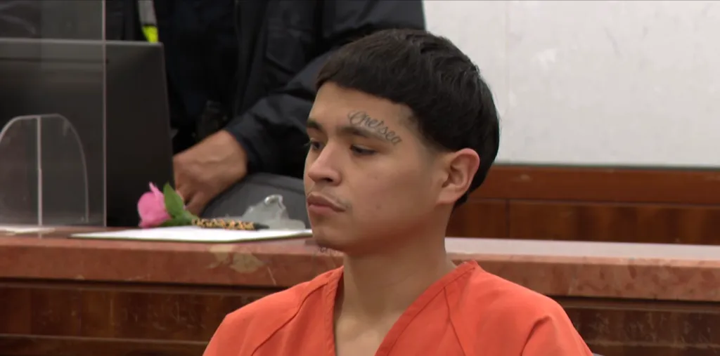 Raudel Orozo in an orange jumpsuit, with a "Chelsea" tattoo above his right eyebrow, sits in a courtroom.