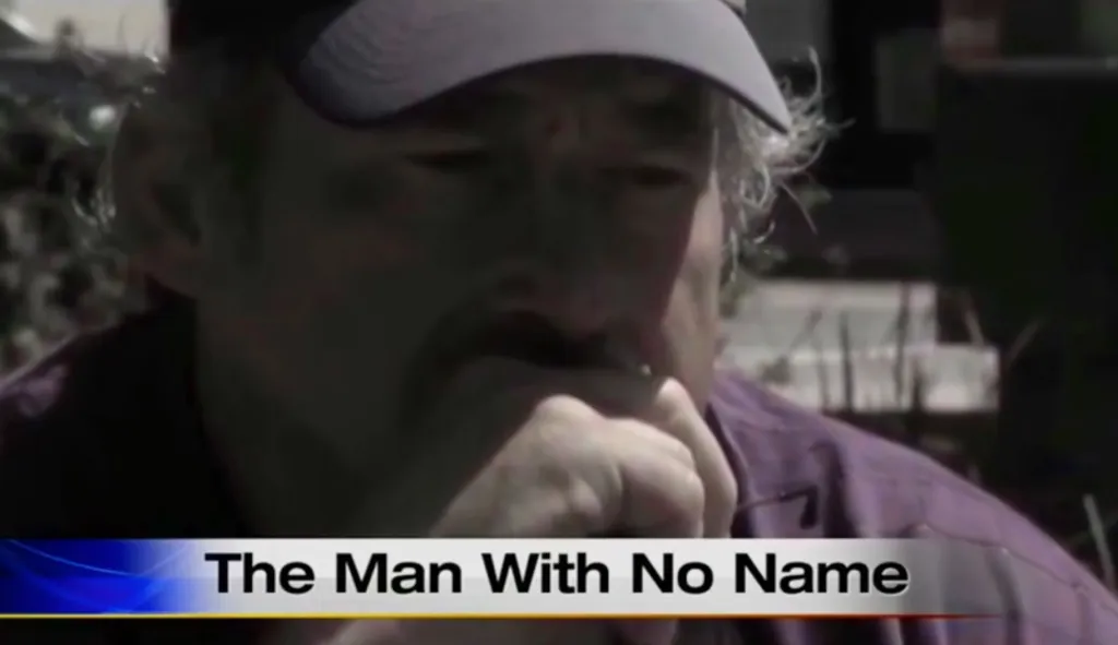Benjaman Kyle, also known as "The Man With No Name," wearing a cap, looking down with his hand on his chin.