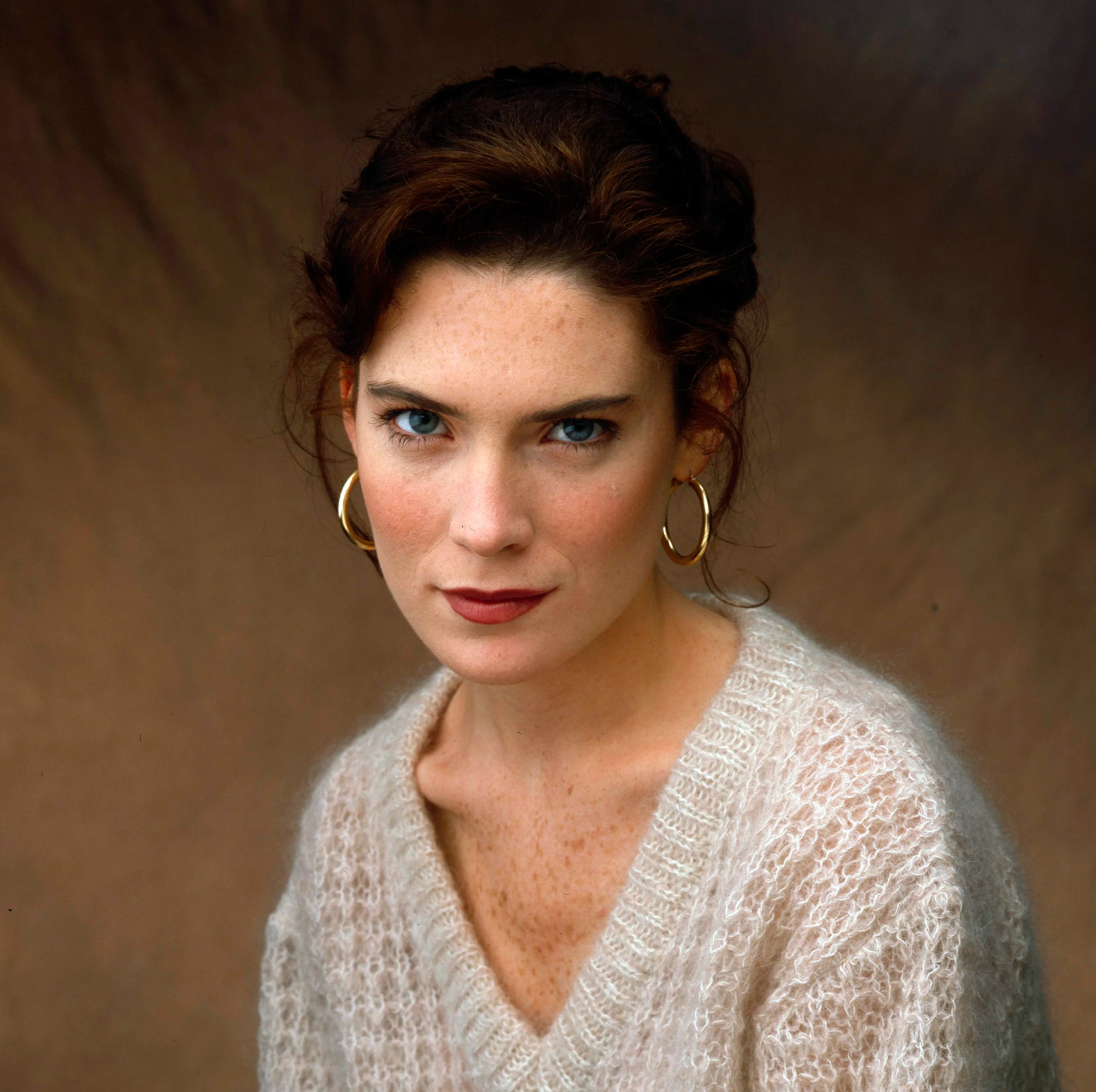 Lara Flynn Boyle wearing a light, fuzzy sweater and gold hoop earrings.