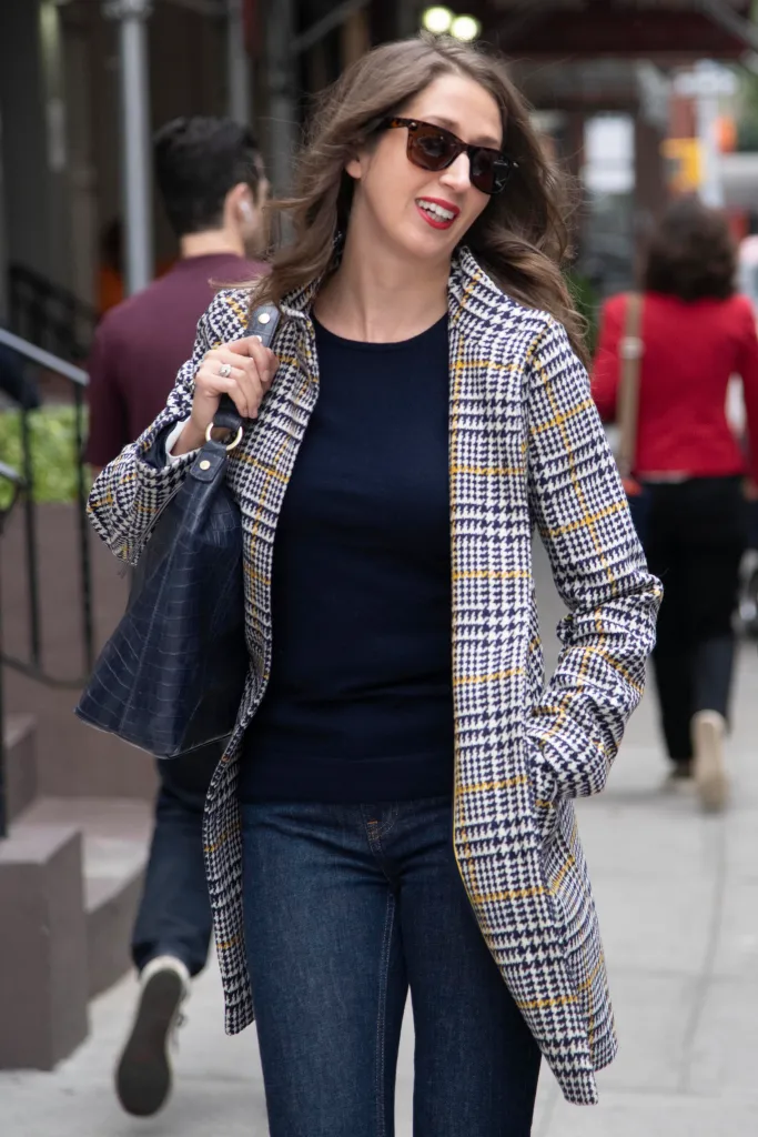 Brooke Nevils walking outdoors in a tartan blazer and sunglasses.