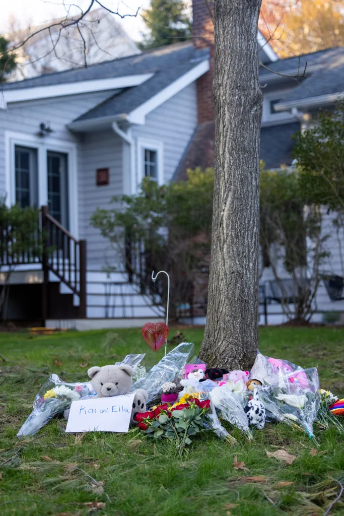 A memorial with flowers, stuffed animals, and a sign reading "Kai and Ella" on a lawn in front of the Wellesley, Massachusetts house where authorities found Kai and Ella MacAusland dead inside