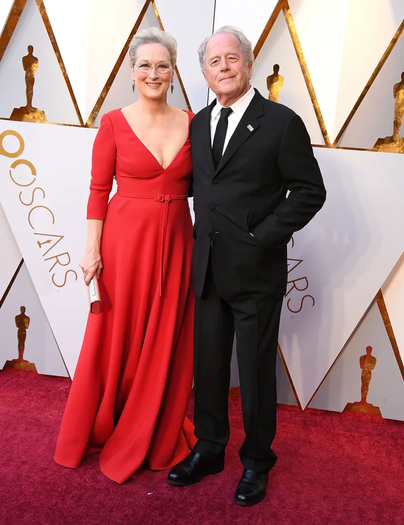 Meryl Streep in a red gown with Don Gummer in a black suit on the red carpet.