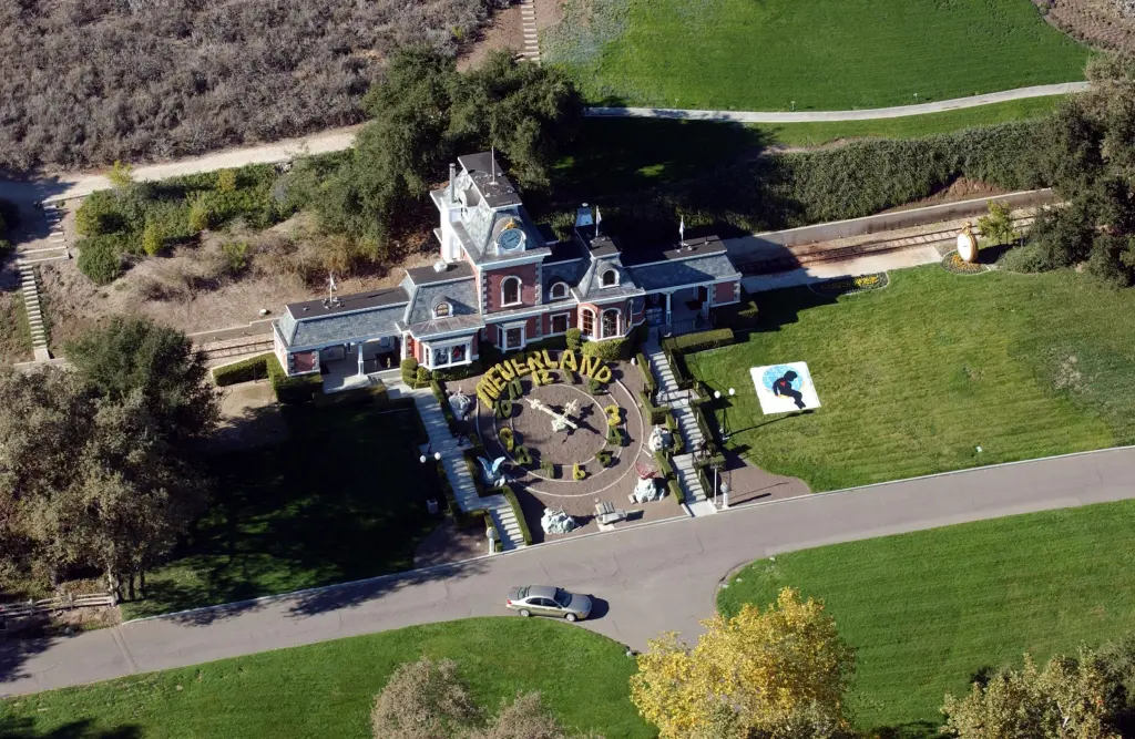 Aerial view of Michael Jackson's Neverland Ranch, showing the main building, clock made from bushes, and a car parked on an adjacent road.