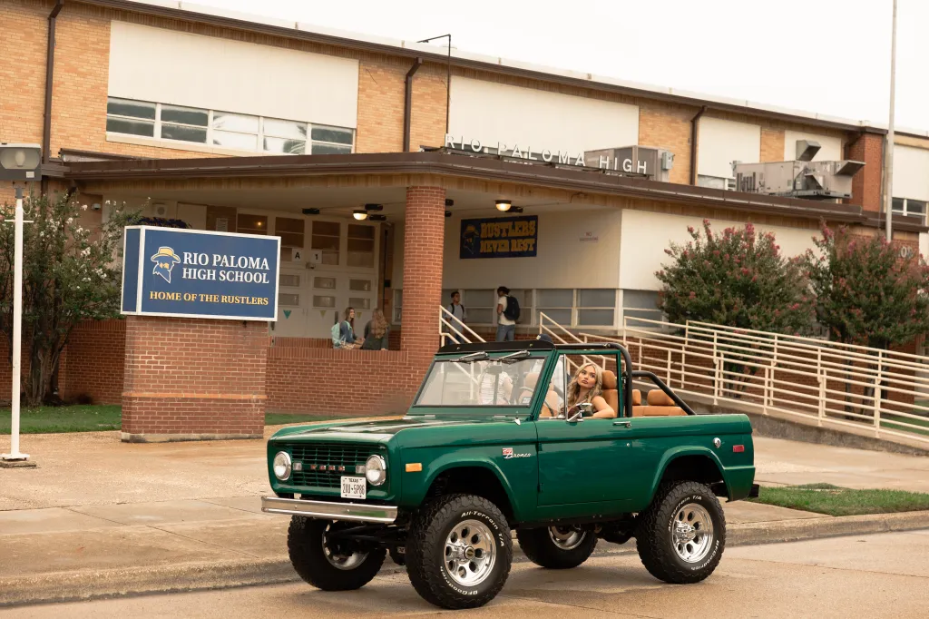 Natalie Alyn Lind as Oreana in a green Ford Bronco in front of Rio Paloma High School.