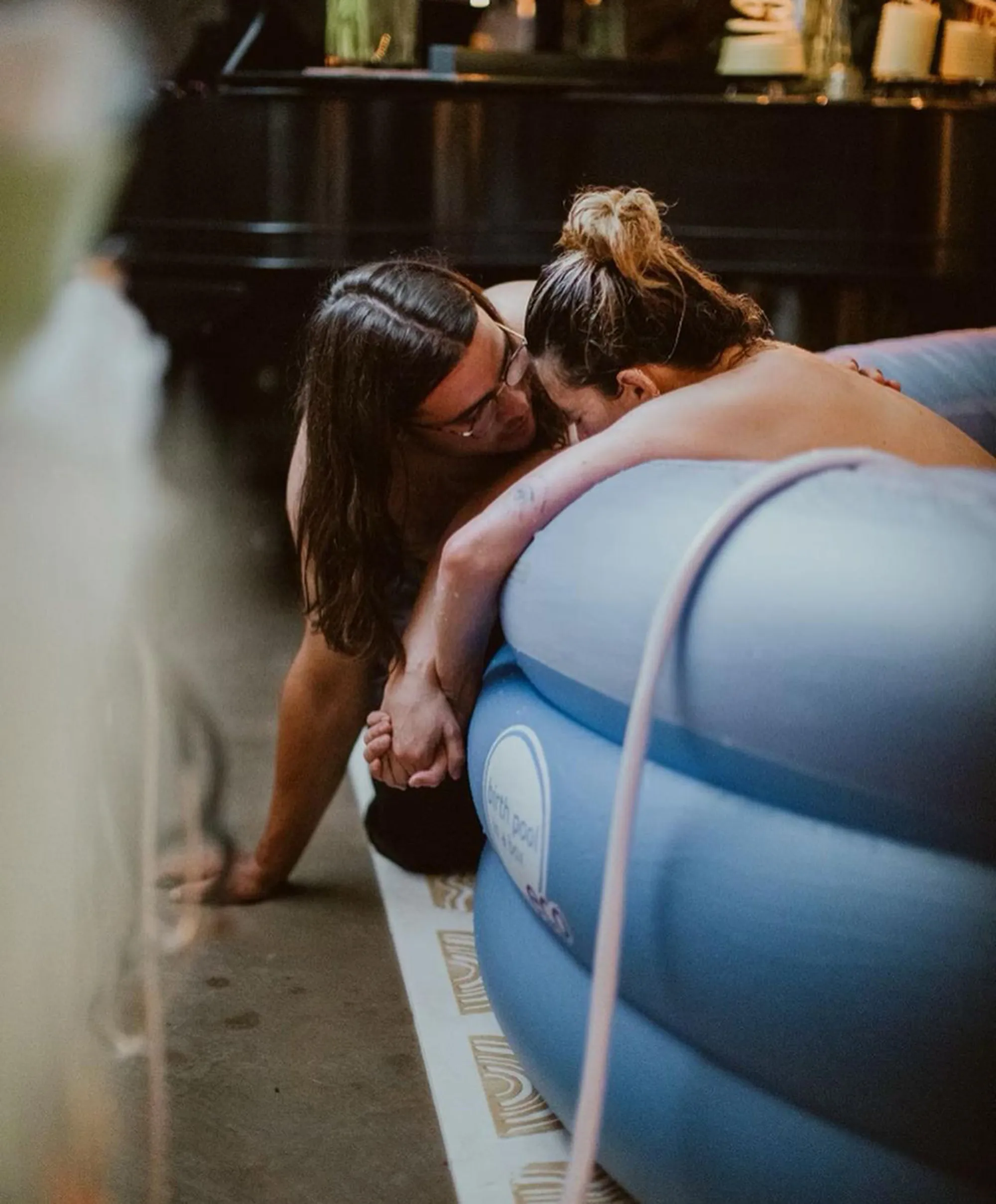 A man with long hair and glasses holding the hand of a woman in a birth pool.