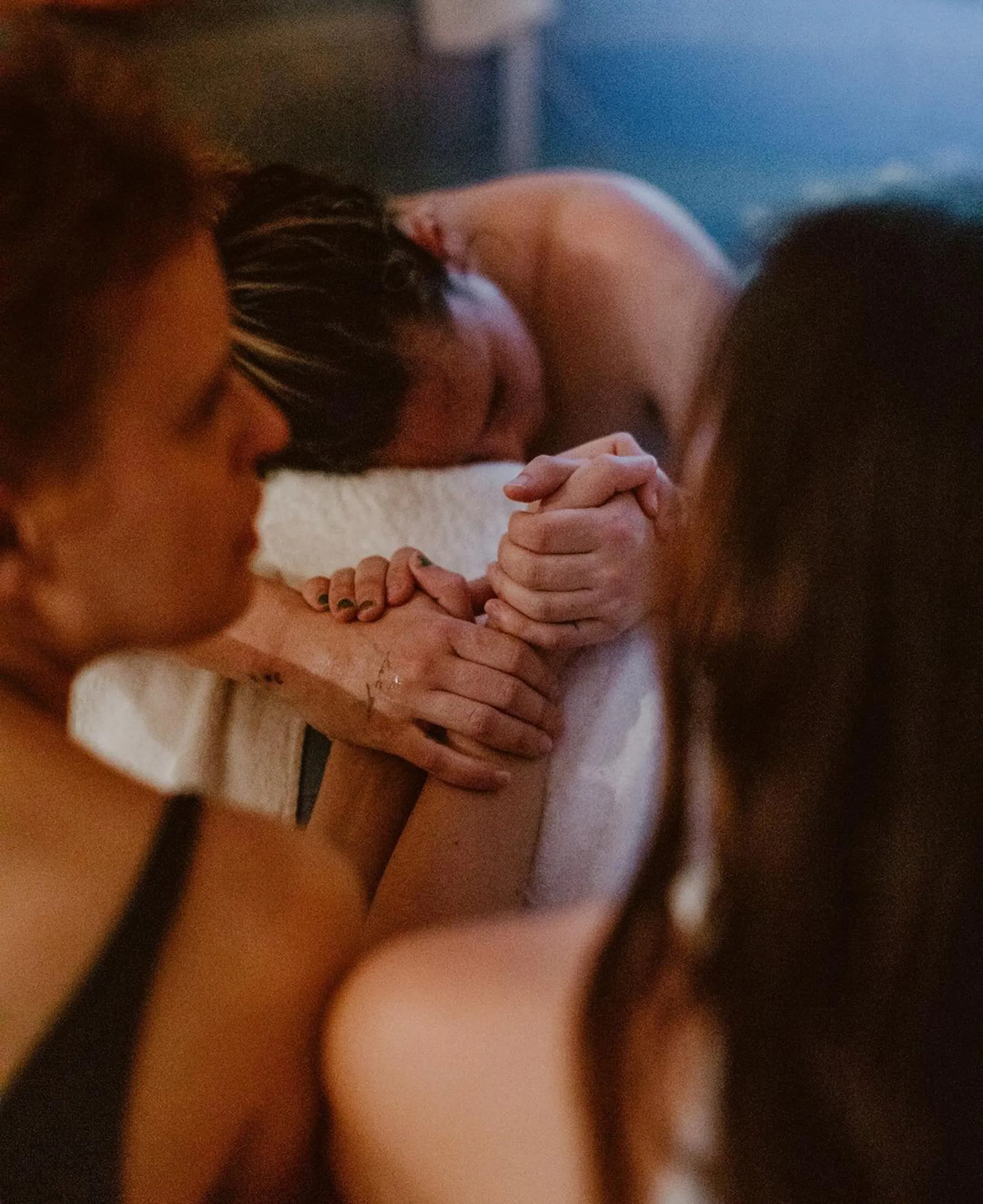 A person holding hands with another person who is lying down with their head bowed.