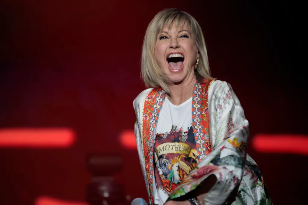 Olivia Newton-John on stage, singing with her mouth wide open.