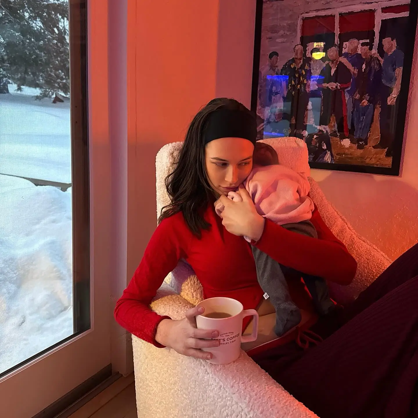 Elsie Hewitt holding a baby, while holding a mug.