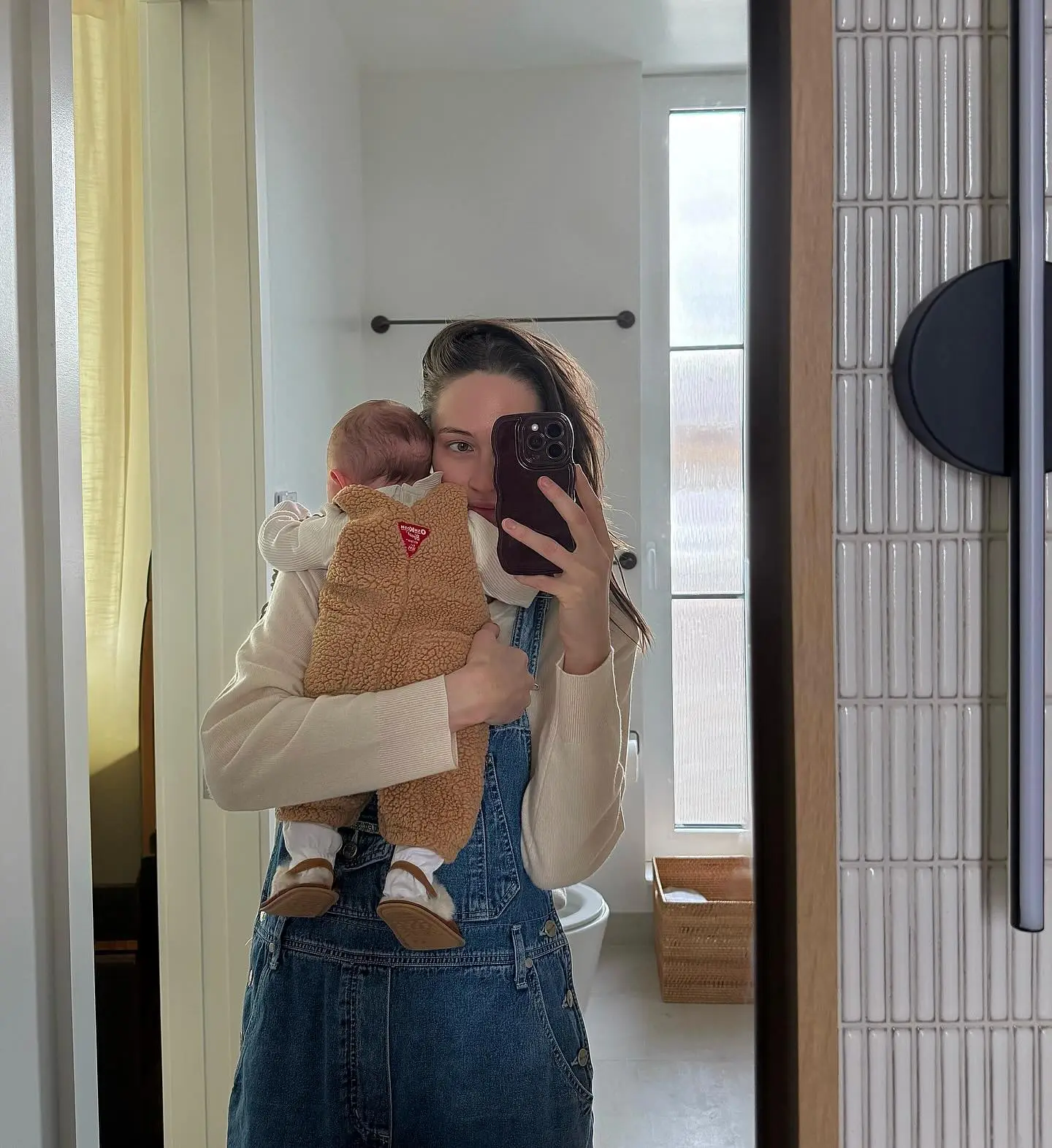 Elsie Hewitt holding a baby, taking a mirror selfie.