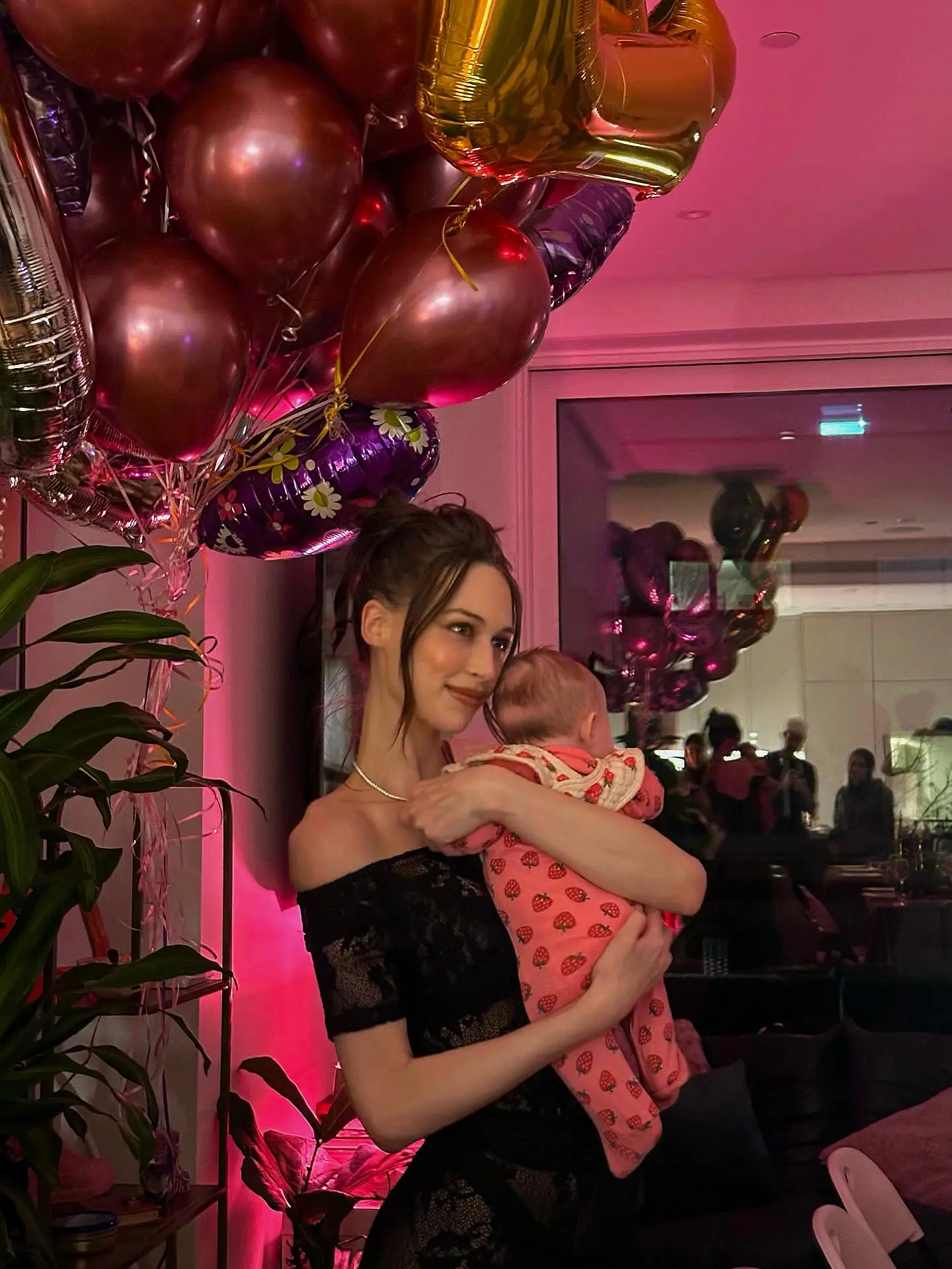 Elsie Hewitt holding a baby, surrounded by balloons.
