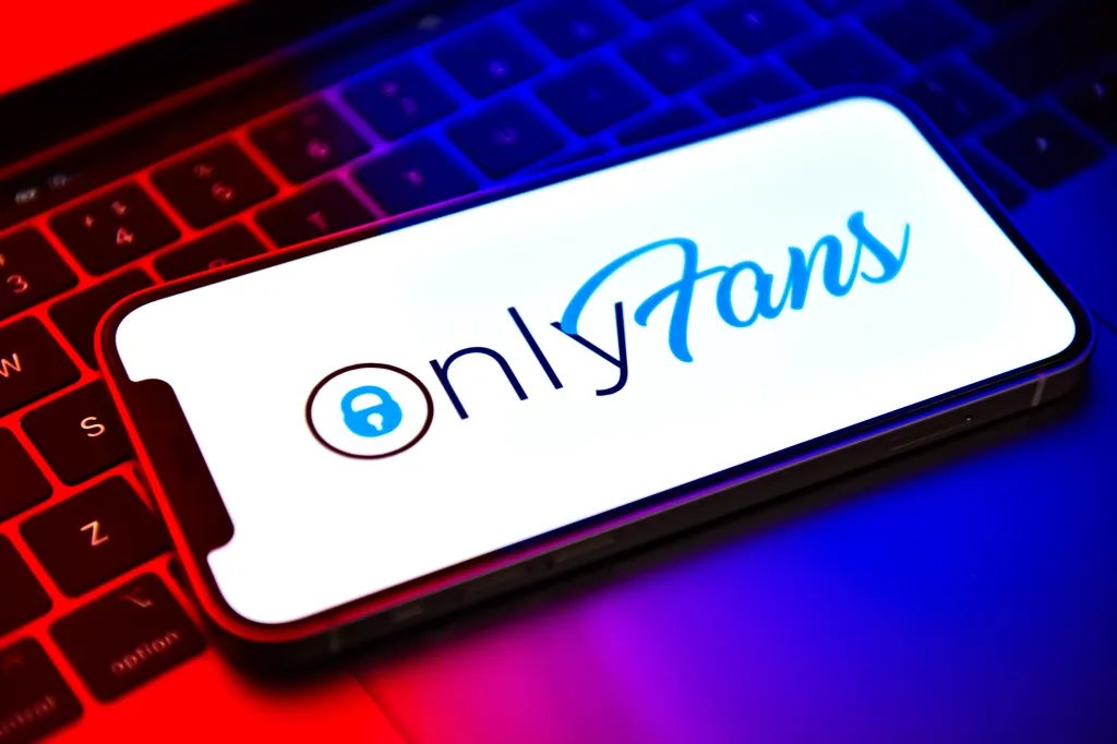 Illustration of the OnlyFans logo displayed on a smartphone screen, resting on a keyboard lit with red and blue light.