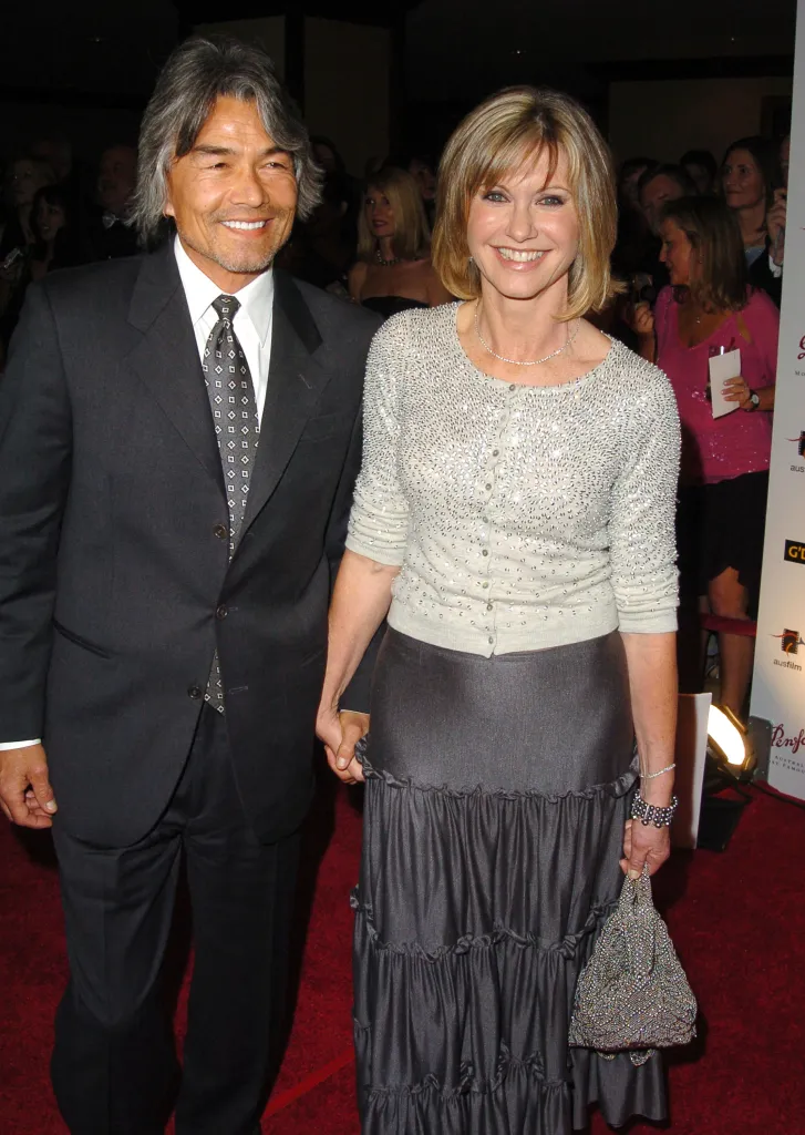 Olivia Newton-John and Patrick McDermott smiling and holding hands at a red carpet event.