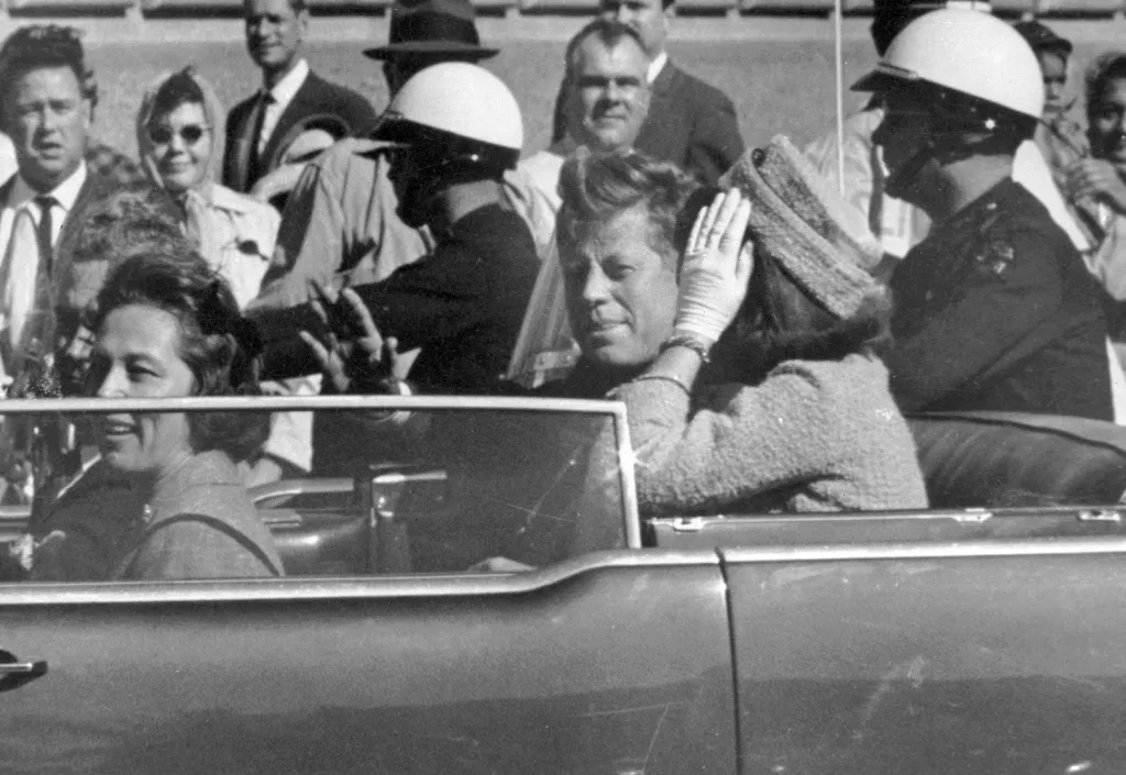 President John F. Kennedy waves from his car in a motorcade in Dallas.