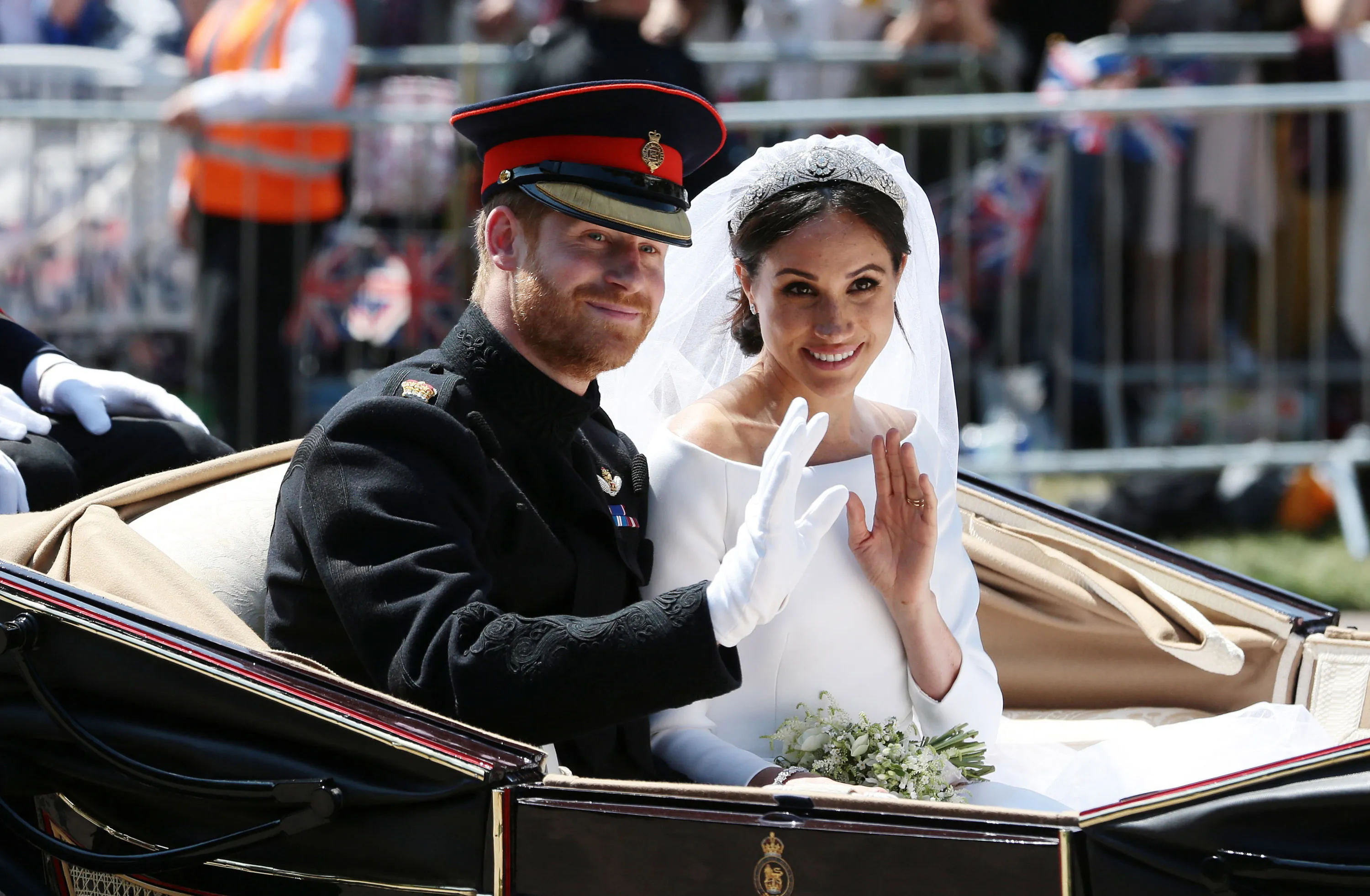Prince Harry and Meghan Markle waving from a carriage during their wedding procession.