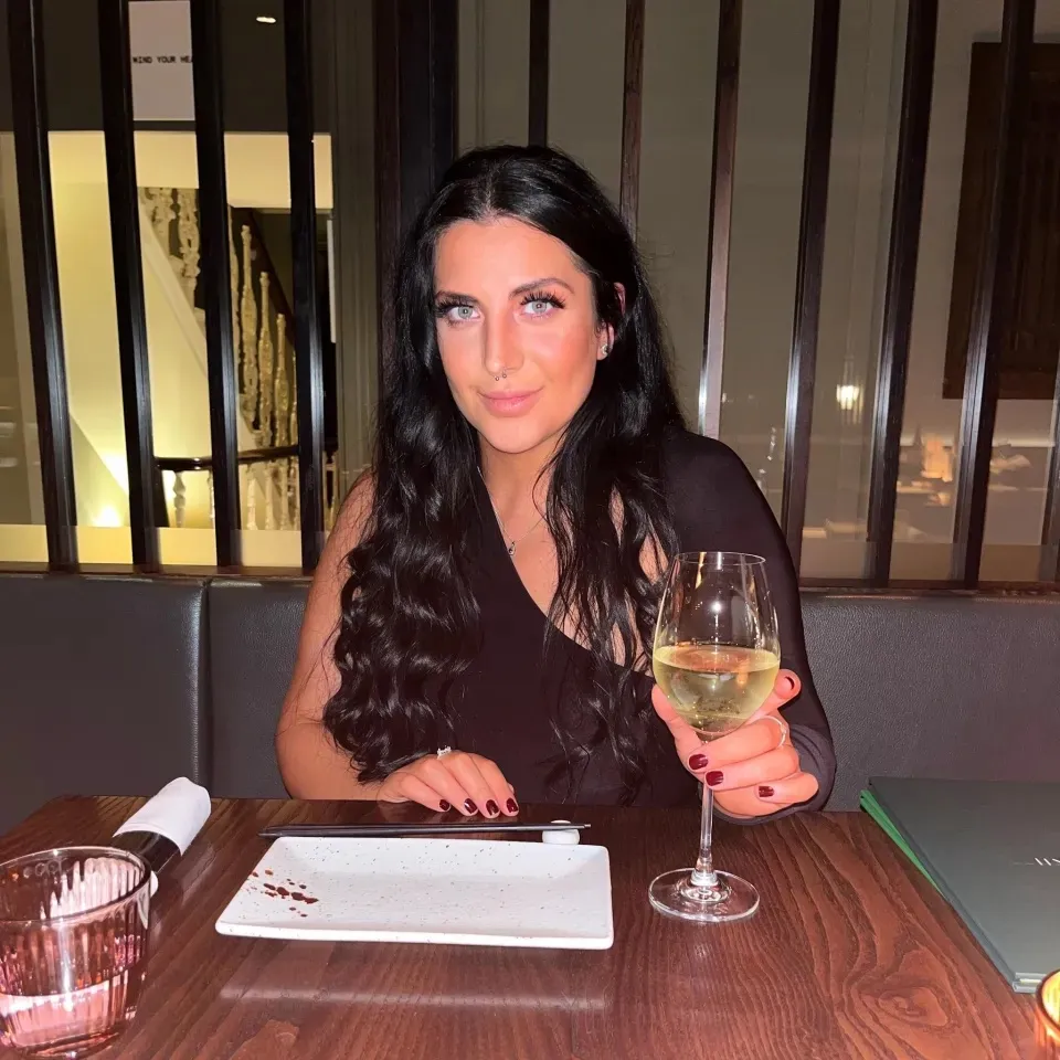 Michelle Molver sits at a restaurant table, holding a glass of white wine.