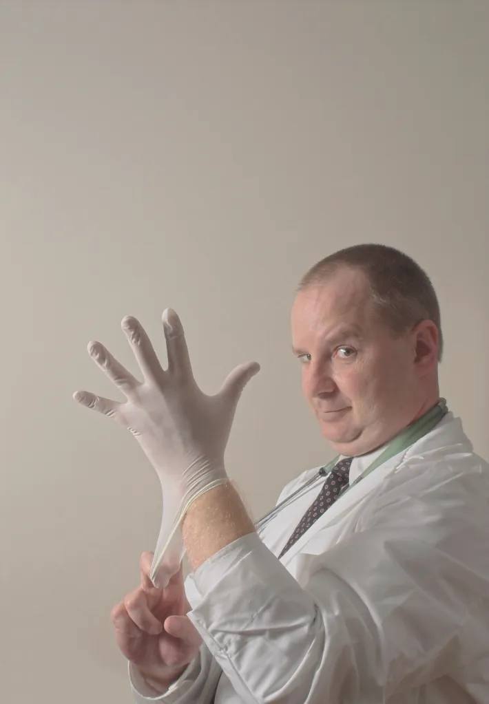 A proctologist putting on a rubber glove for an examination.