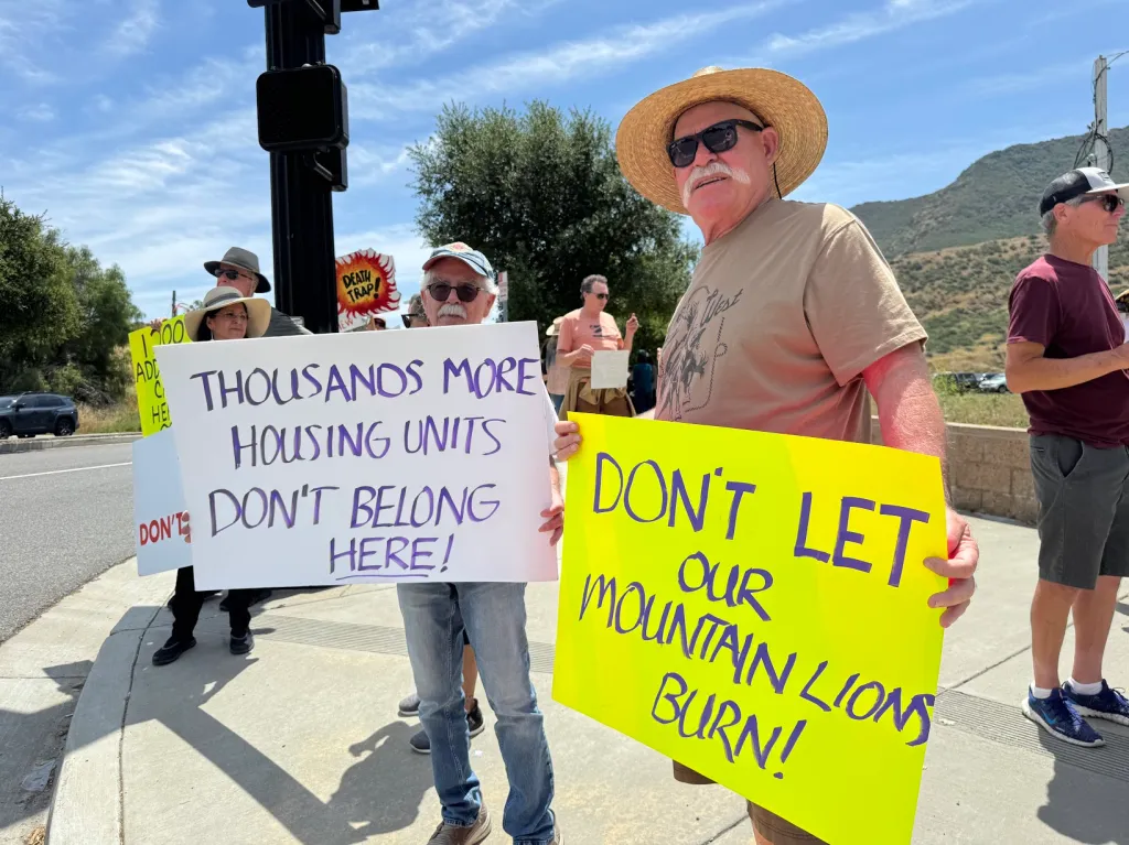Protestors hold signs opposing new housing units, with signs reading 