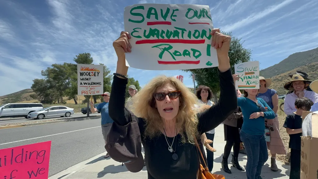 A woman holding a sign that says "SAVE OUR EVACUATION ROAD!" at a protest in Agoura Hills.