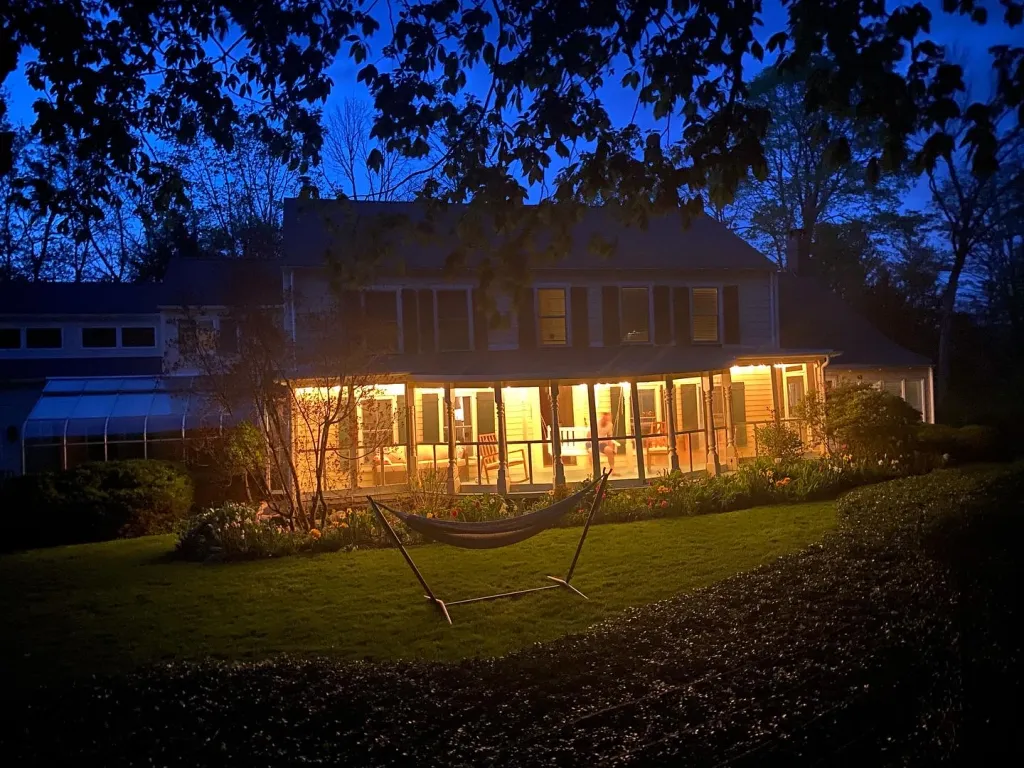 A brightly lit house with a hammock in the front yard at dusk.