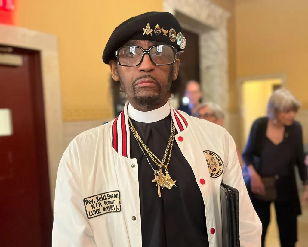 Rev. Keith Gadson wearing a white jacket with an "Innocence Project" patch and "Rev. Keith Gadson N.I.P. Founder Luke 4:18(KJV)" patch.