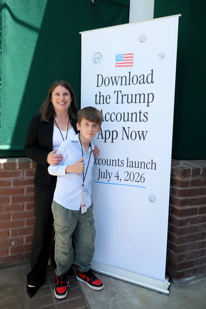 Robin D. Shapiro and her son Marty stand next to a "Download the Trump Accounts App Now" banner.