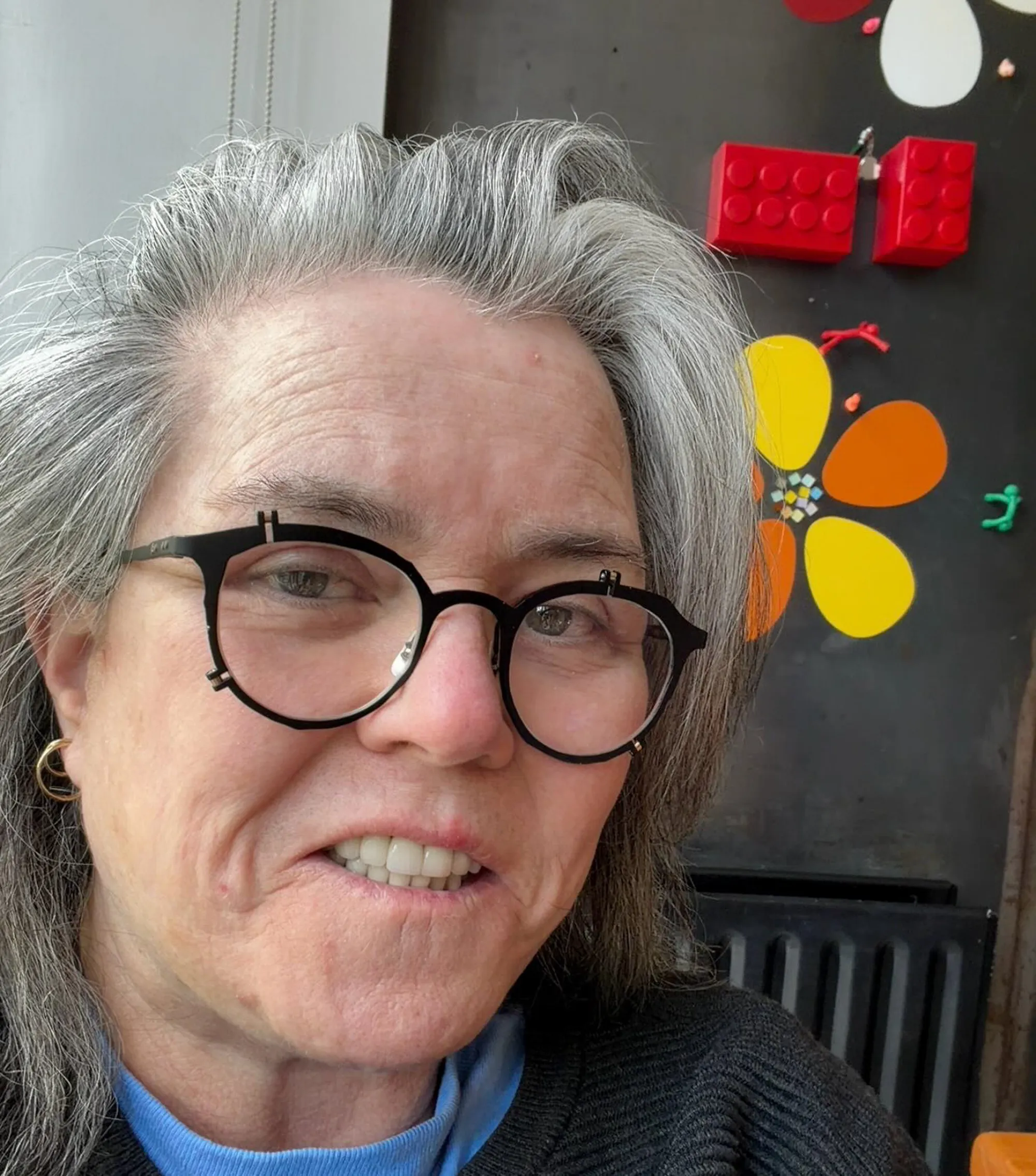 Rosie O'Donnell in black glasses with gray hair.