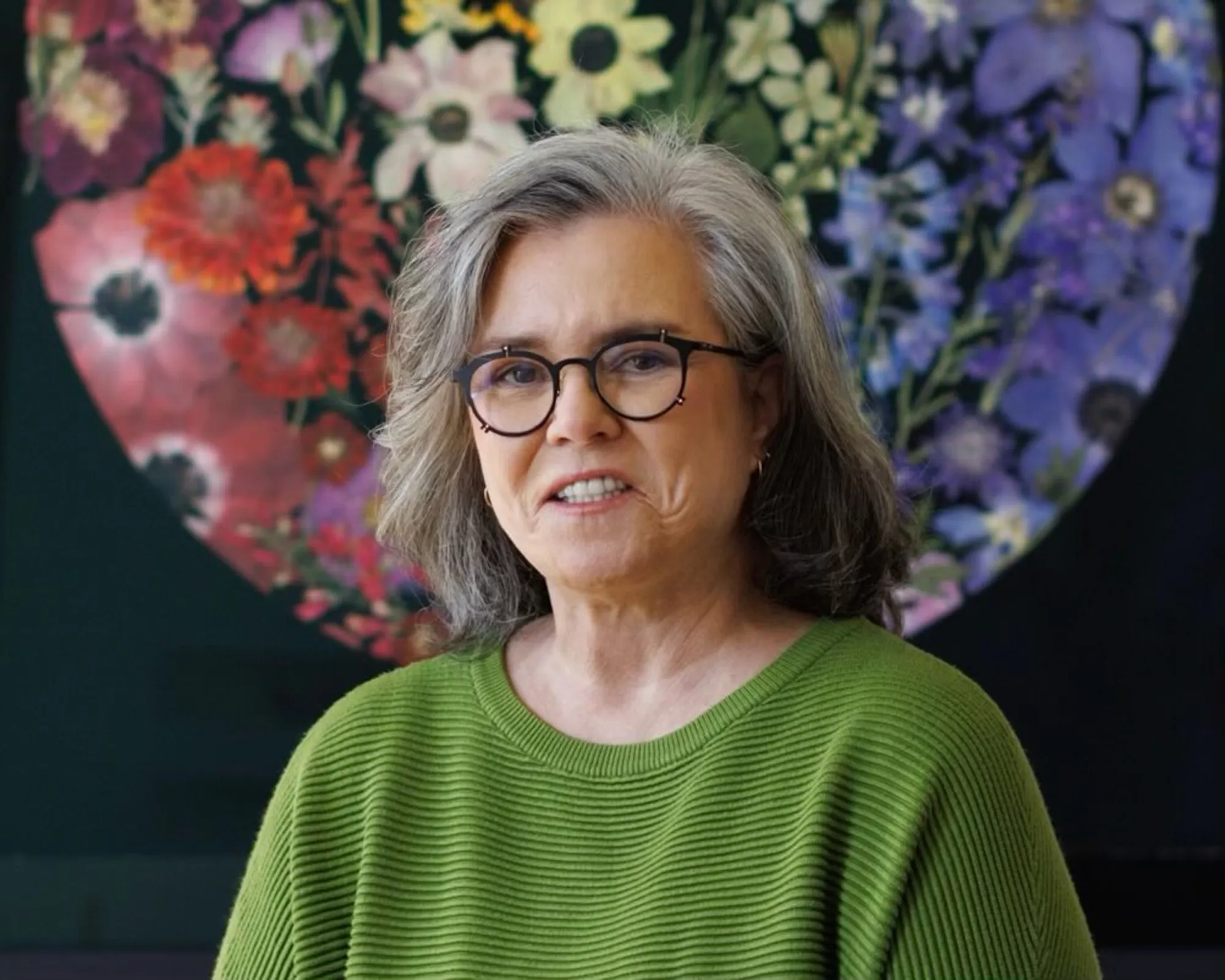 Rosie O'Donnell wearing glasses and a green shirt, speaking about her facelift.