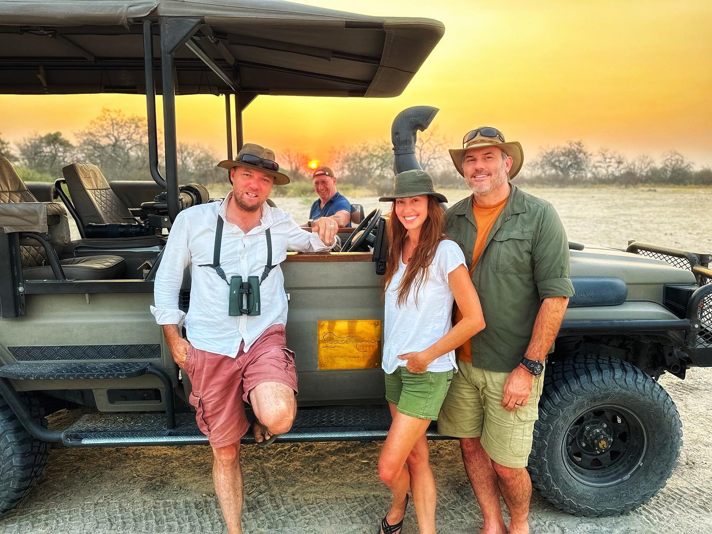 Shannon Elizabeth and her husband Simon Borchert posing with a safari vehicle at sunset in Moremi Game Reserve, Okavango Delta, Botswana.