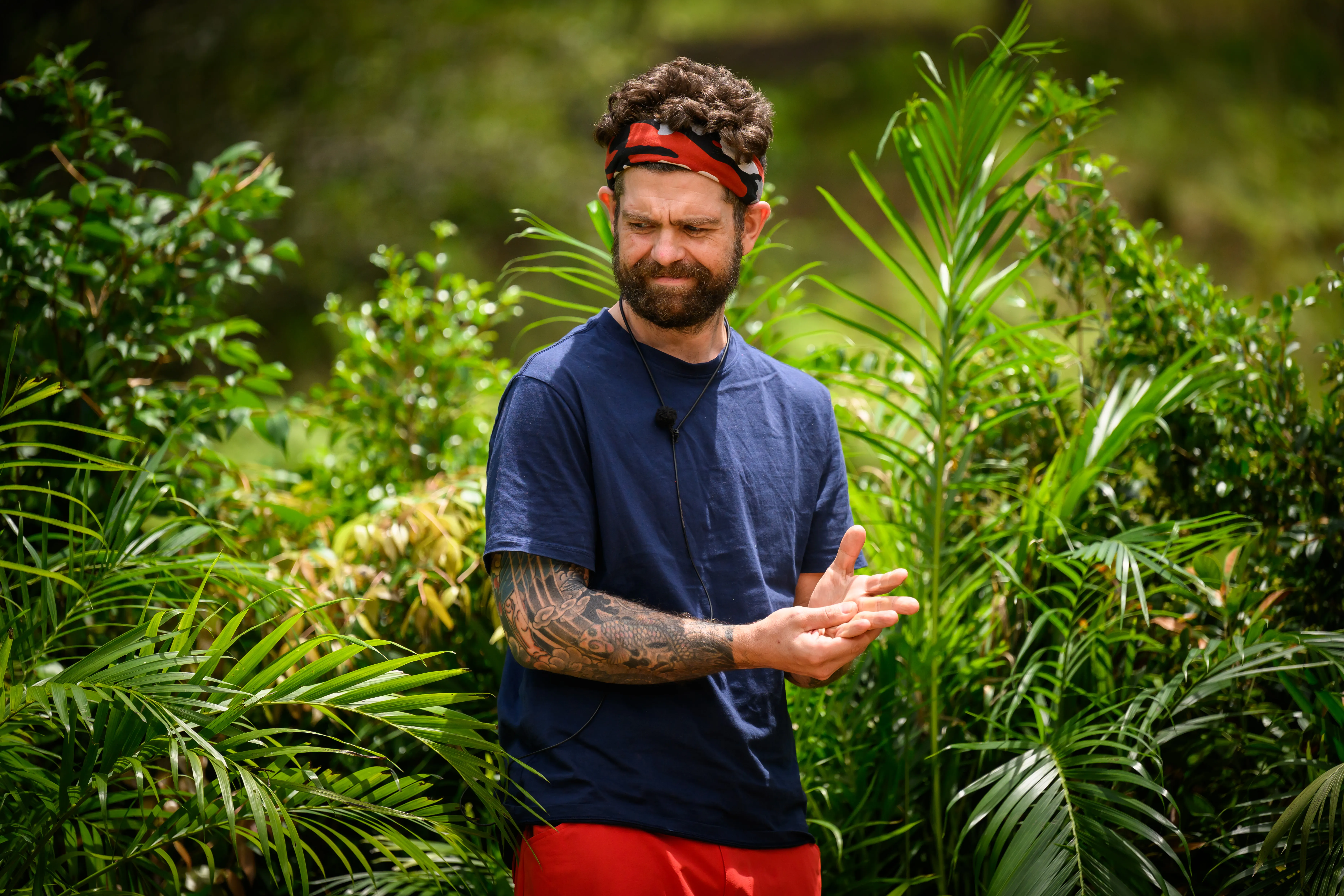Jack Osbourne wearing a red bandana and red shorts, standing in a jungle for the show I'm a Celebrity... Get Me Out of Here!