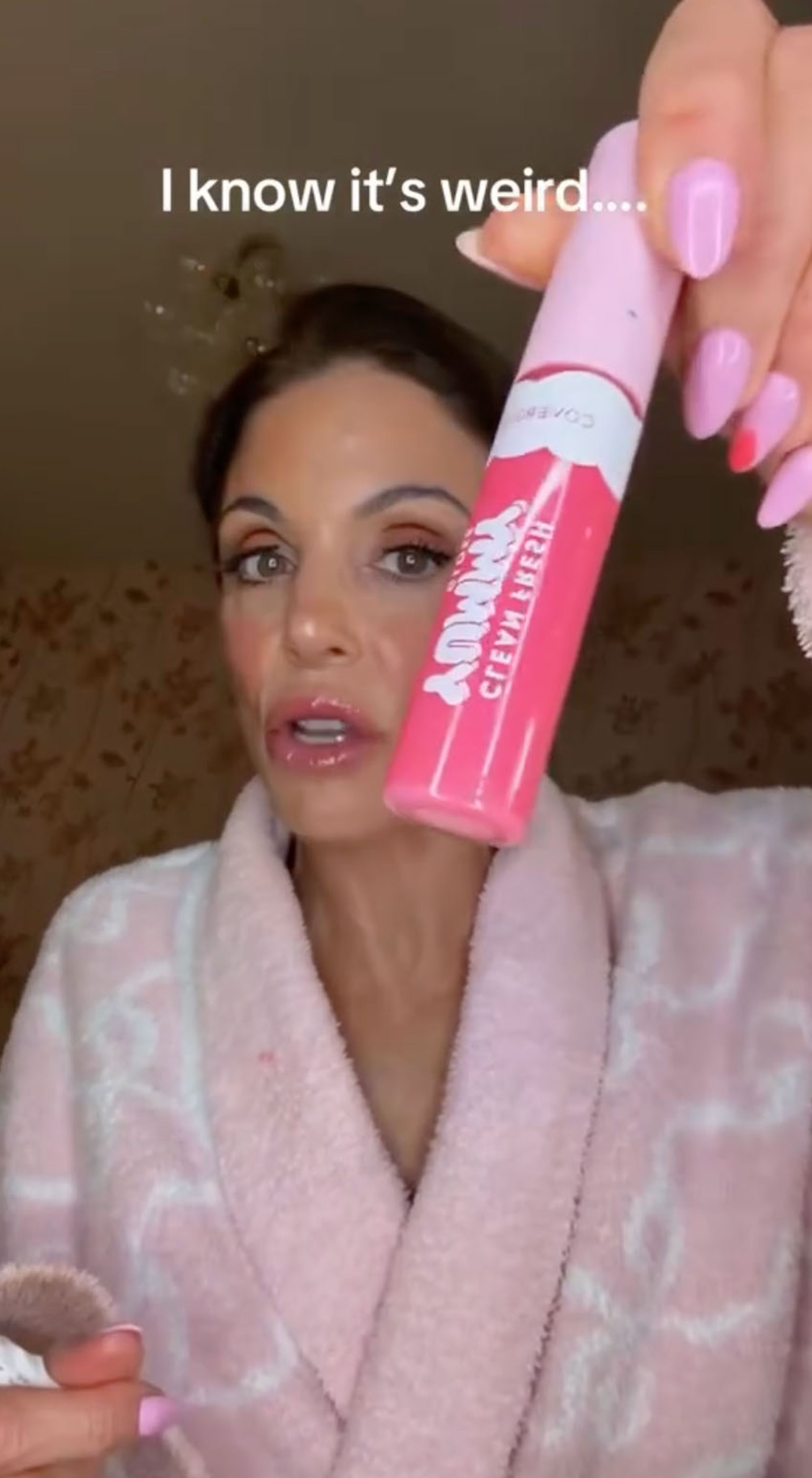 A woman in a pink robe holds up a pink lip gloss bottle that reads "YUMMY."