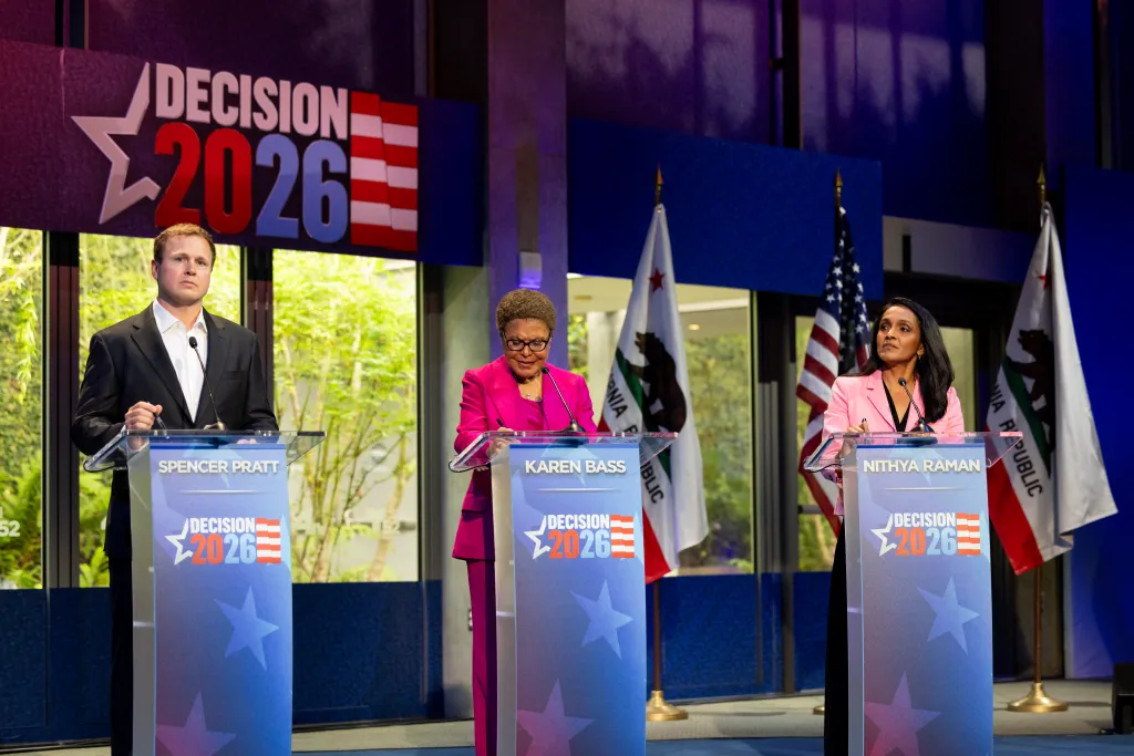 Spencer Pratt, Mayor Karen Bass, and Nithya Raman speaking at a debate with "Decision 2026" branding.