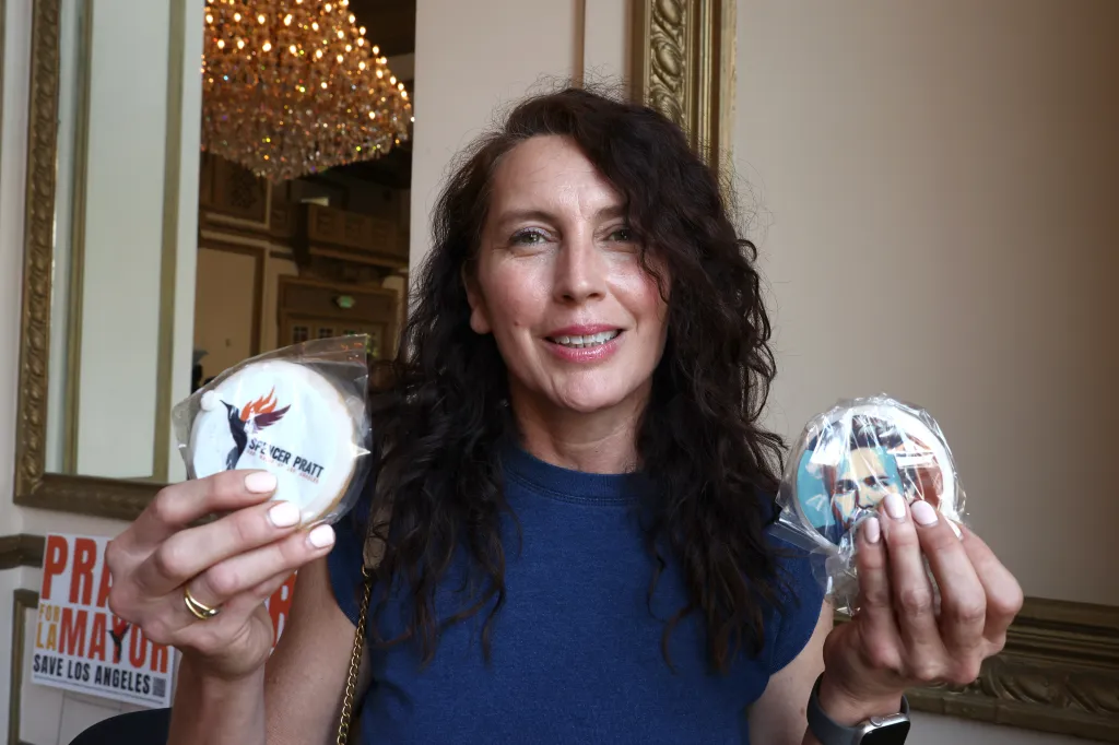 A woman holding two cookies, one for "Spencer Pratt for Mayor" and another with a stylized portrait of him.